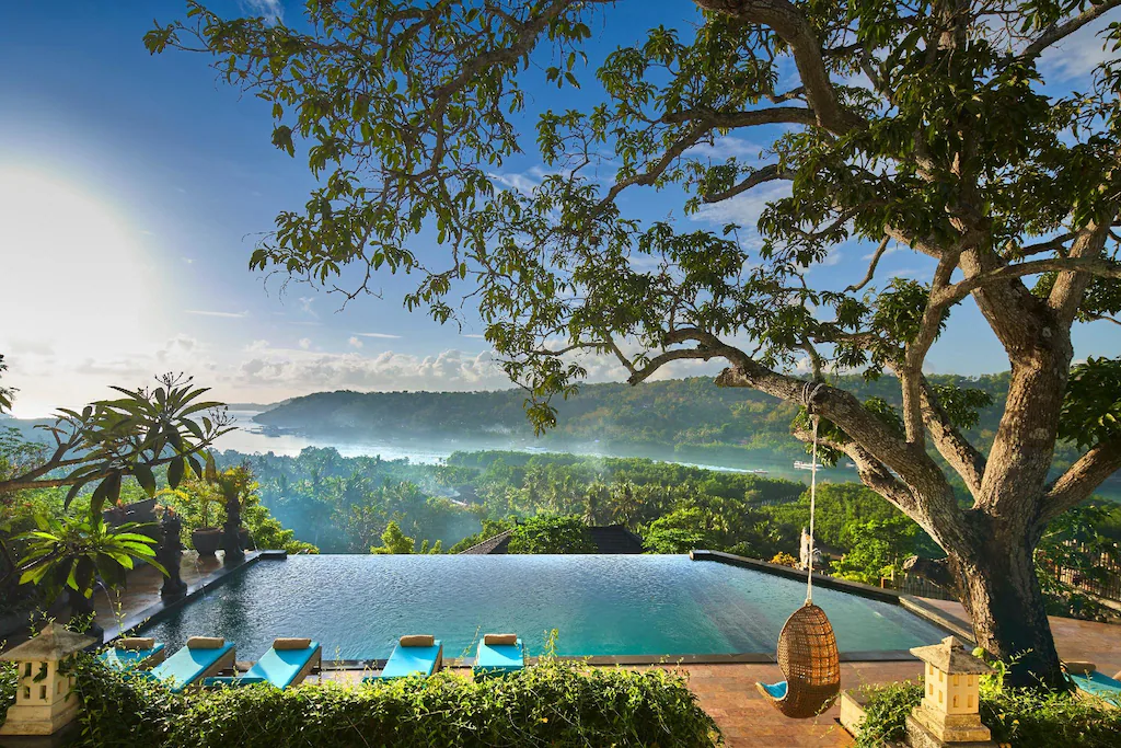 Early morning view of an infinity pool above the tree tops with fog in the background, one of the best places to stay on Nusa Lembongan.