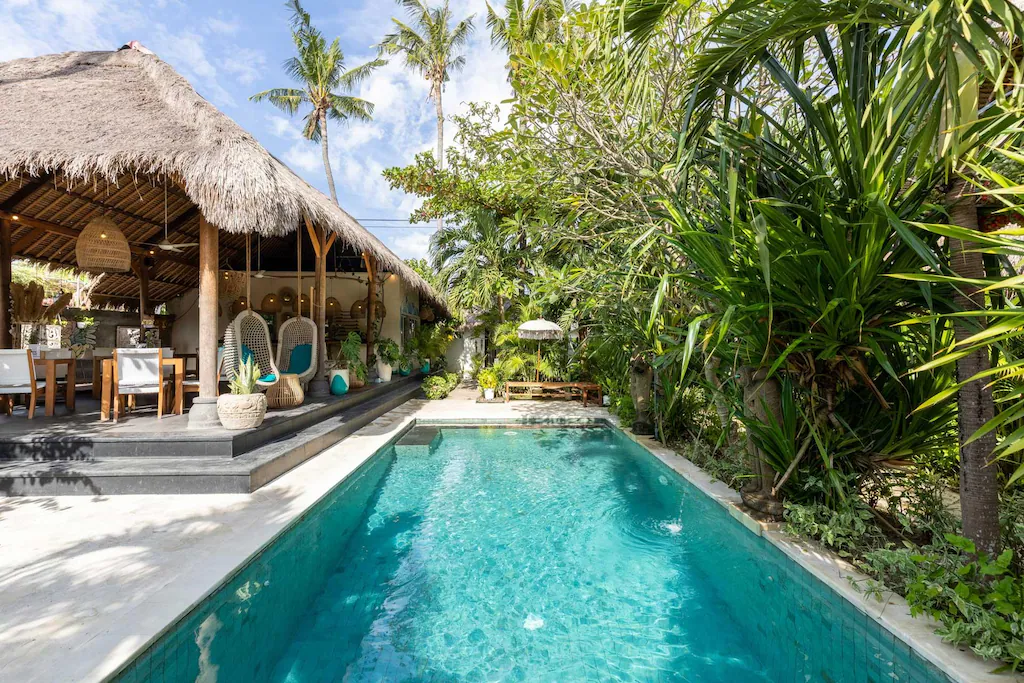 Pool with a bohemian restaurant with a straw roof and lush green garden at Tigerlilly's, one of the best boutique hotels in Nusa Lembongan.