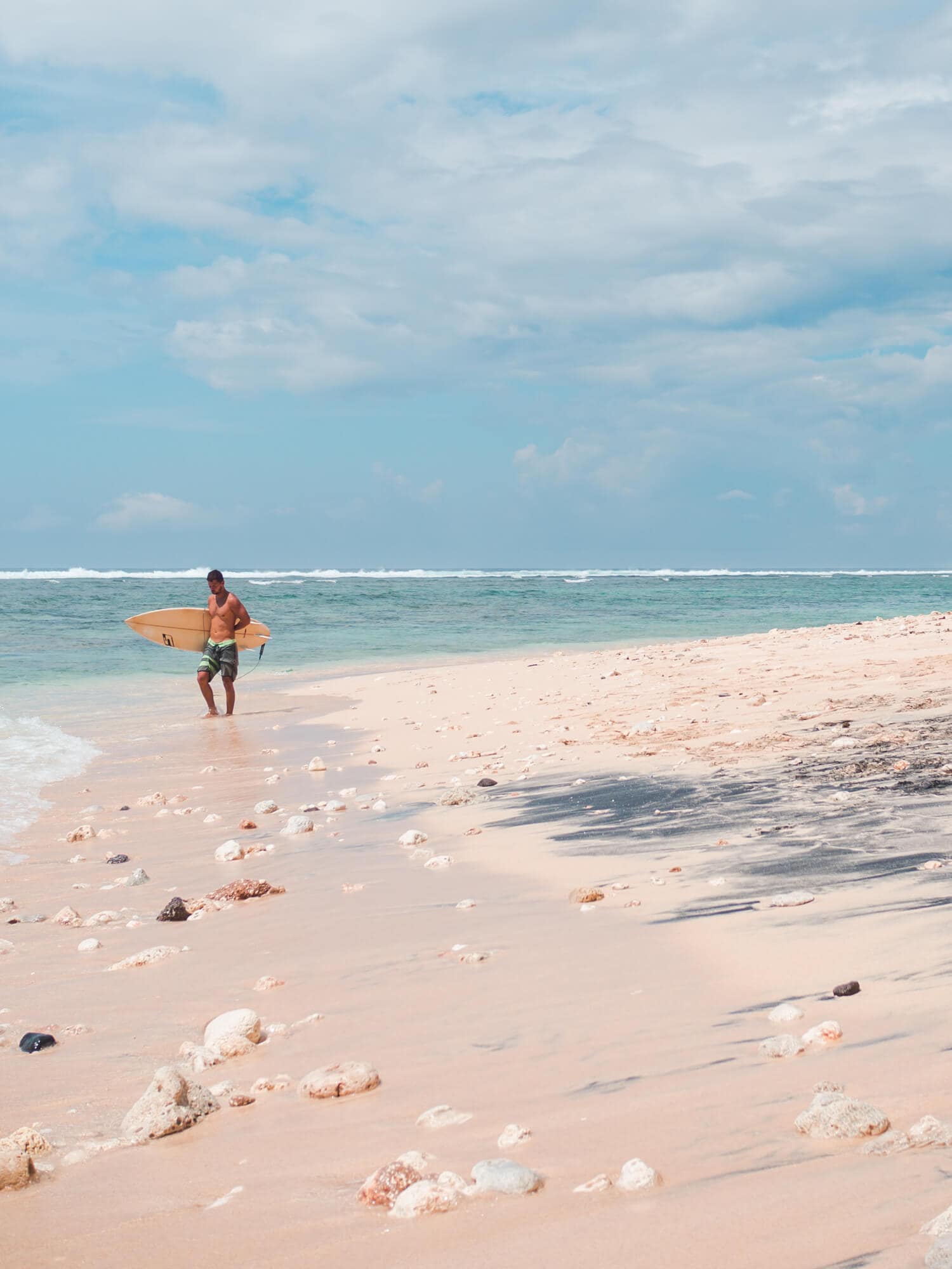 Surfer with a yellow surfboard walking towards the ocean on Green Bow Beach, one of the top things to do in Bali.