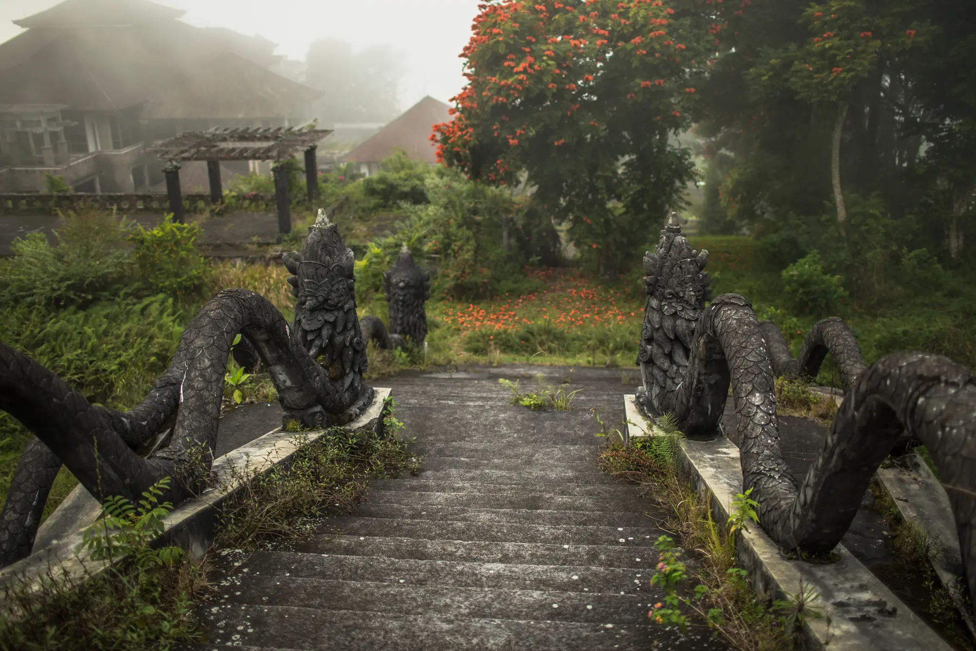 Stone staircase with a dragon on each side leading down to an overgrown garden at the abandoned Taman Rekreasi Resort, one of the top things to do in Bali.