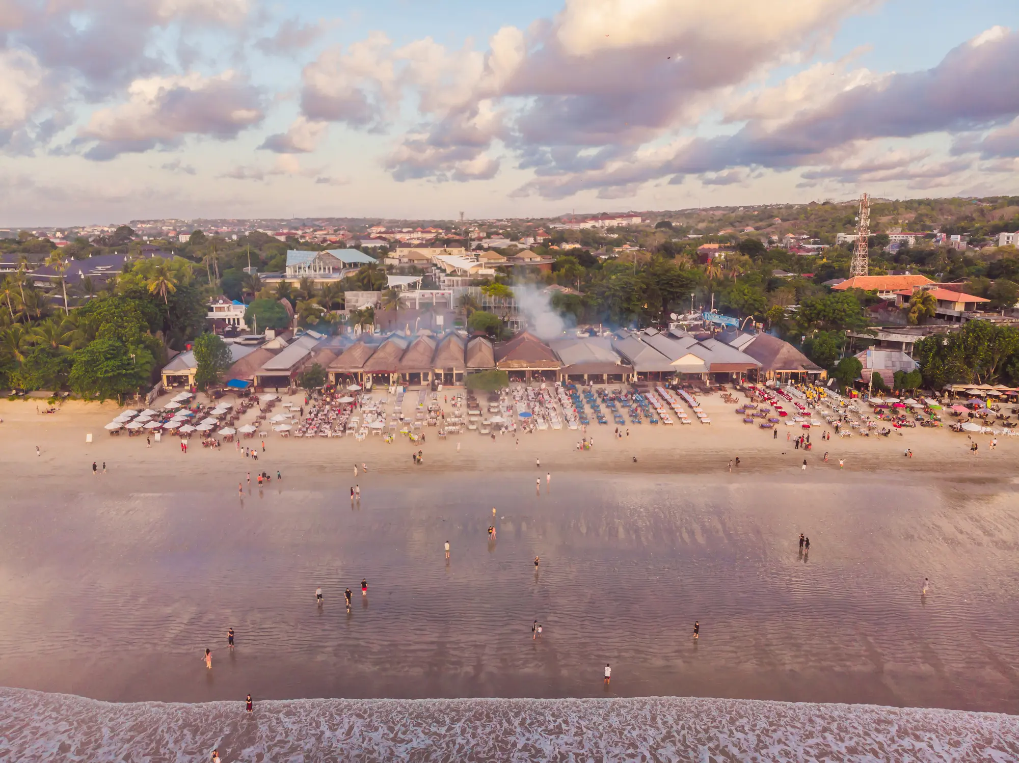 Aerial view of tables and grills in front of warungs on Jimbaran Beach right before sunset, one of the top things to do in Bali.