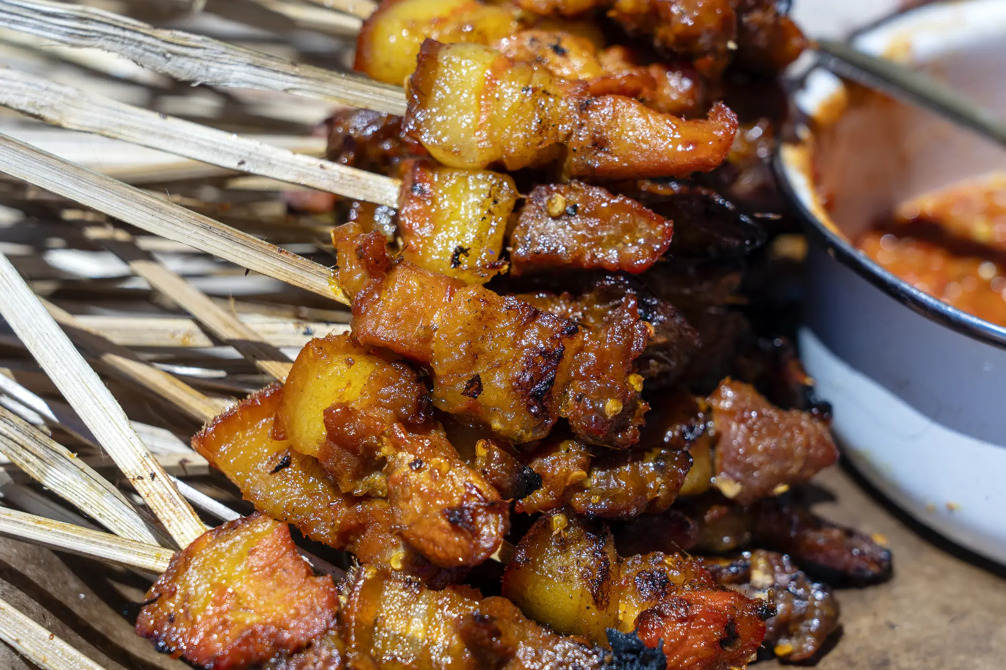 Close up of many pork saté skewers next to peanut sauce at the night market in Sanur, one of the top things to do in Bali.