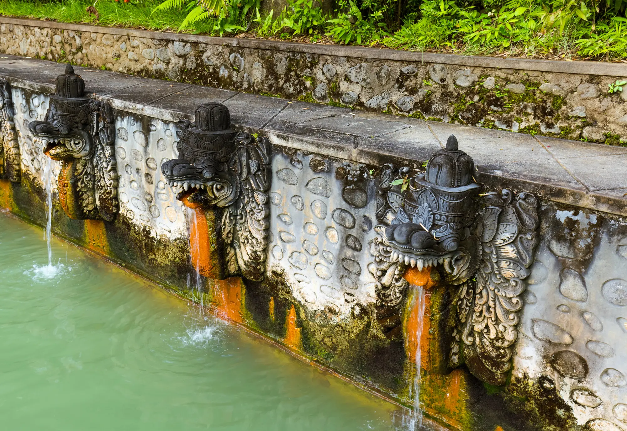 Three stone dragon taps on a wall in the Banjar Hot Springs, one of the top things to do in Bali.