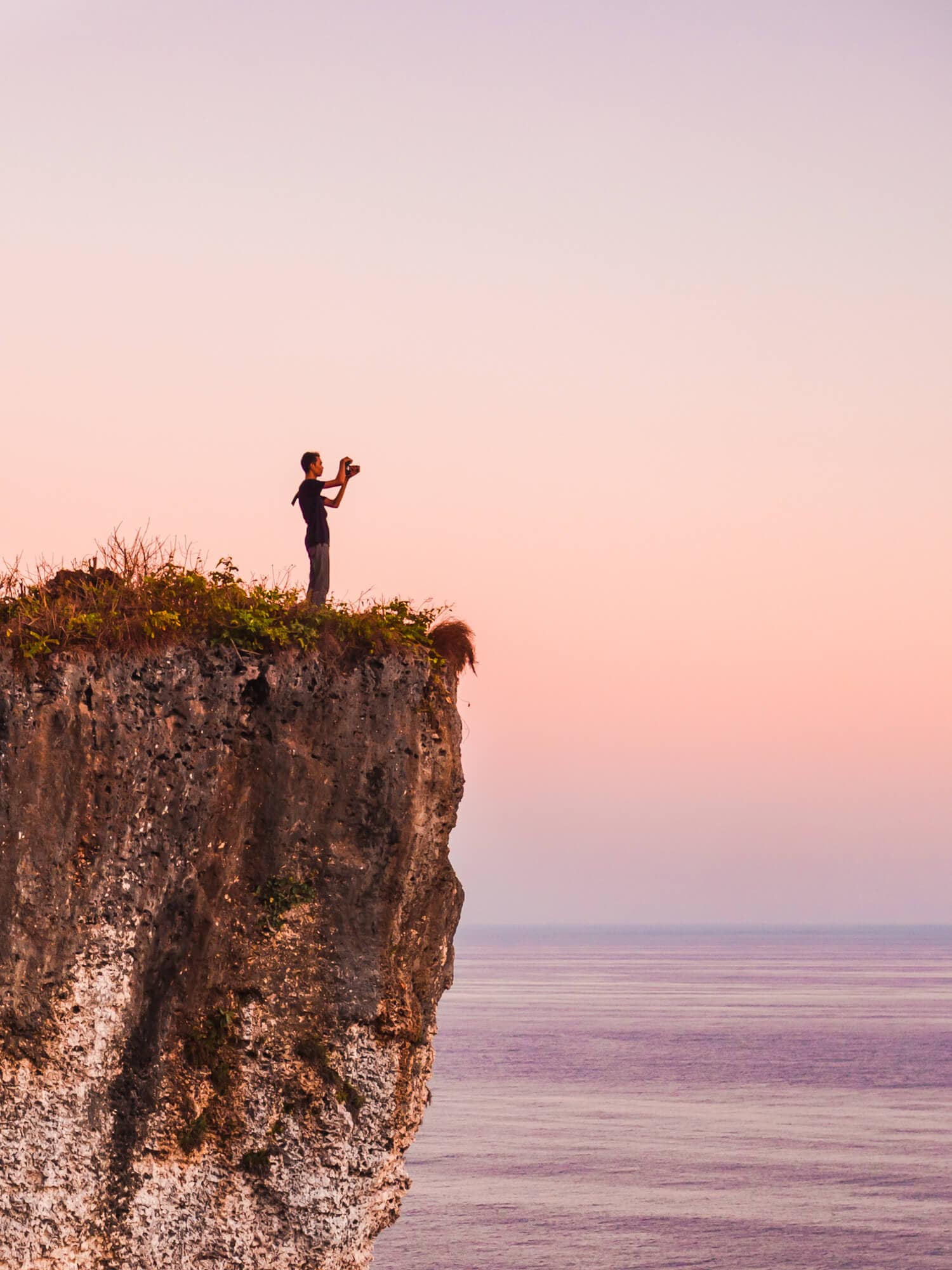 The popular photo spot at Karang Boma Cliff set against a pink and orange sunset