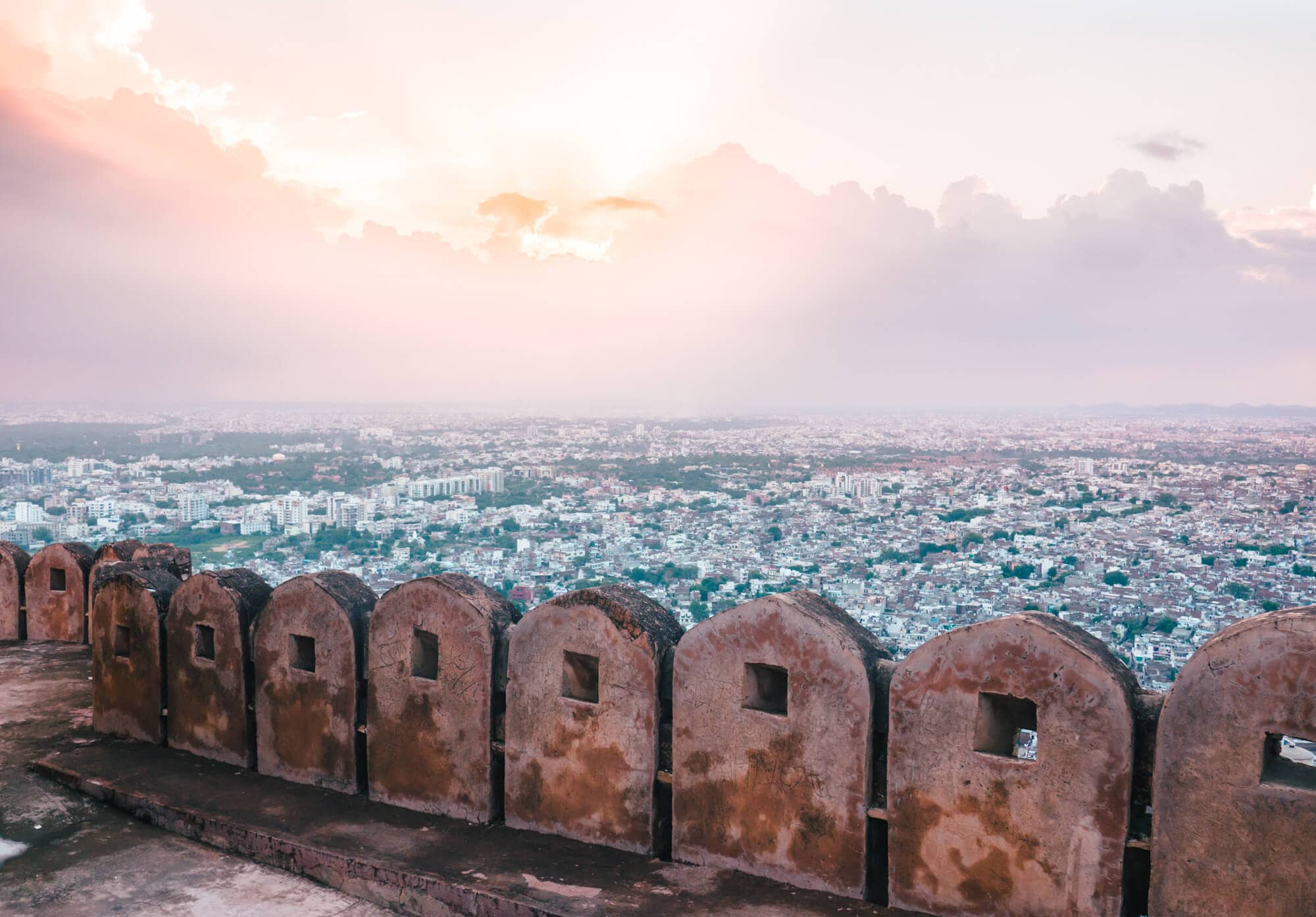 View across Jaipur from the wall of Nahargarh Fort during a pink and yellow sunset.