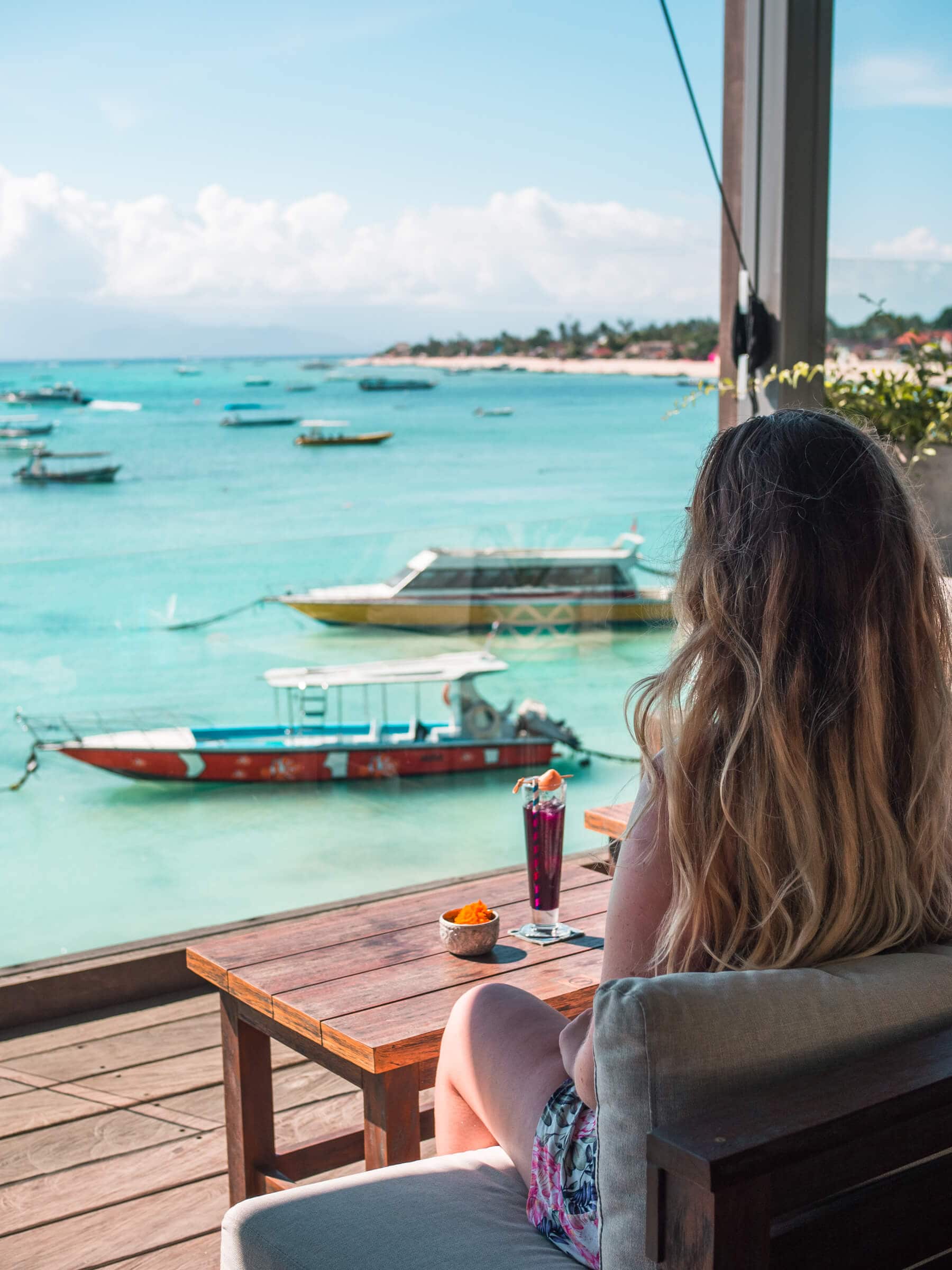 Girl with long hair and a purple drink enjoying the view of turquoise water and Jungut Batu Beach on a day trip to Nusa Lembongan from Bali.