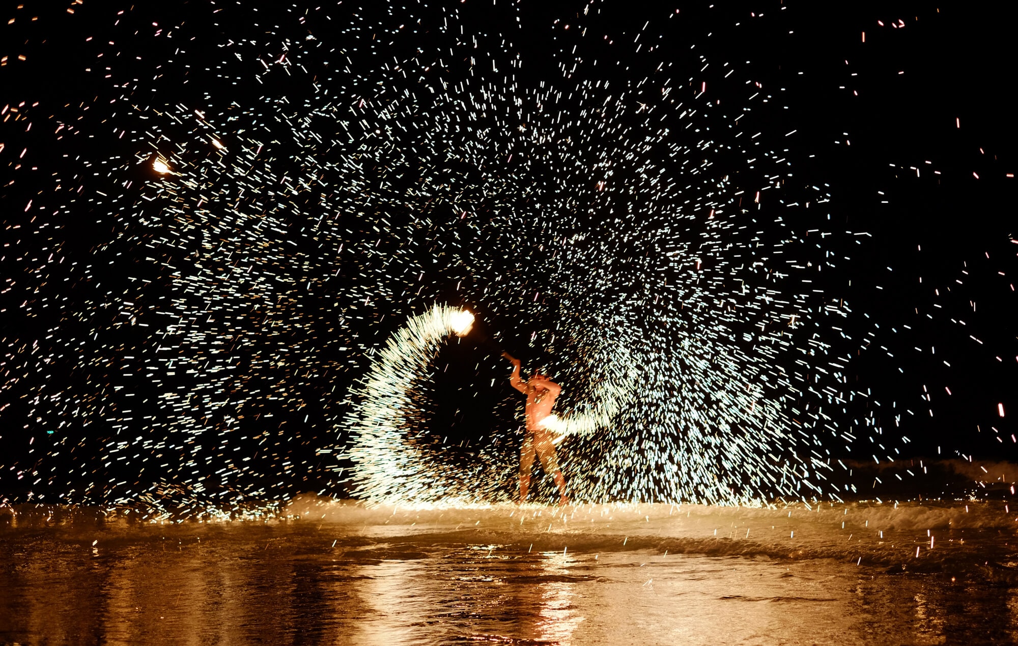 Fire dancer performing on the beach in Koh Samet against a black night sky.