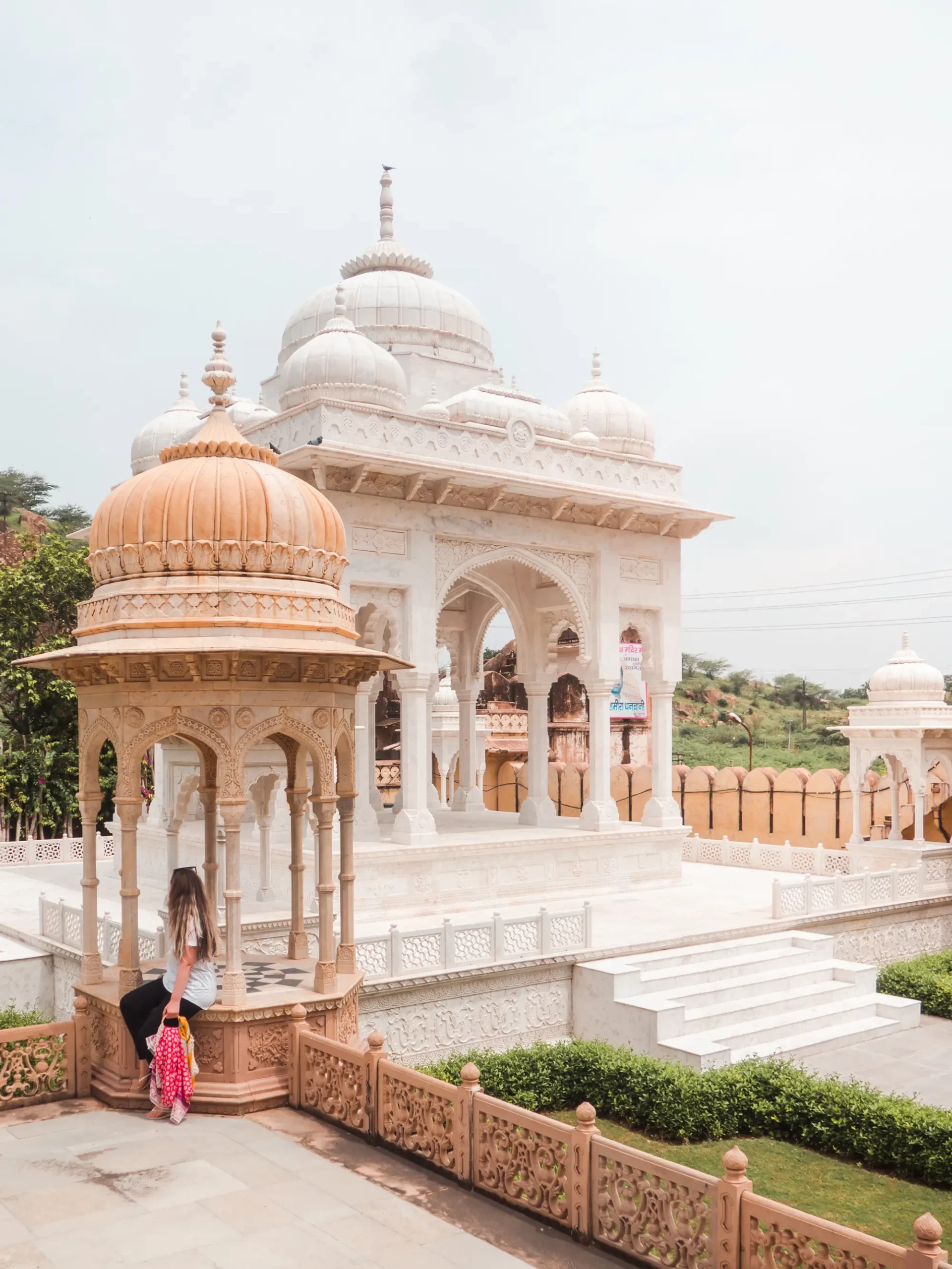 Girl sitting under a ornate beige and white temple at Gatore Ki Chatriyan, during a 2-day itinerary in Jaipur, India. 