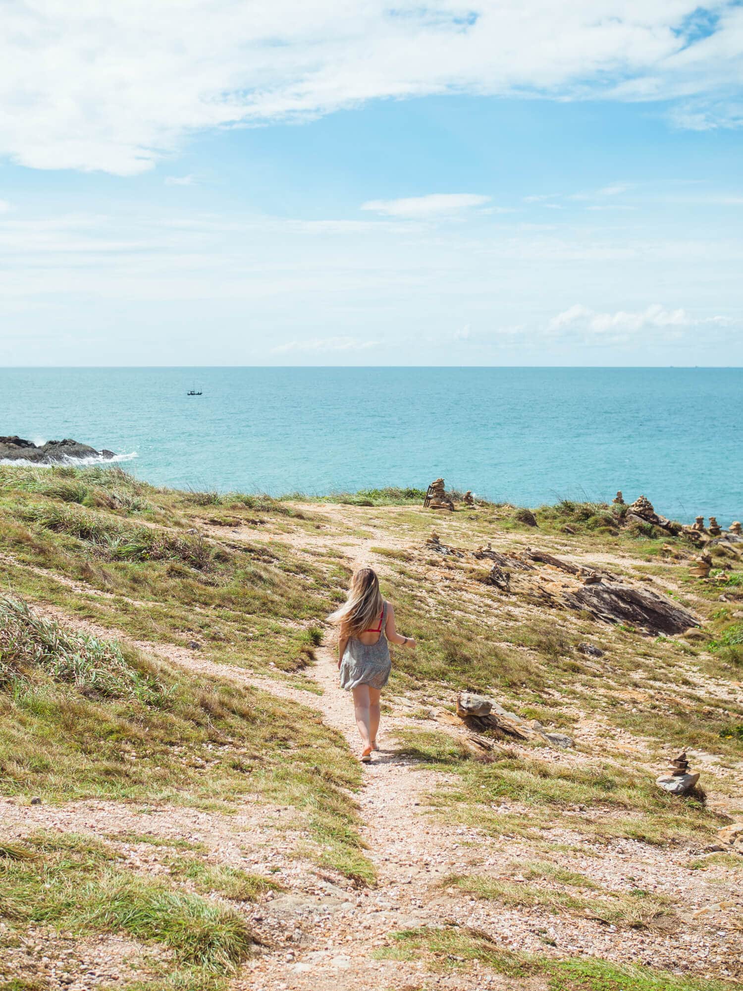 Girl walking down a dirt path towards the ocean and Leam Toei, the southernmost point of Koh Samet.