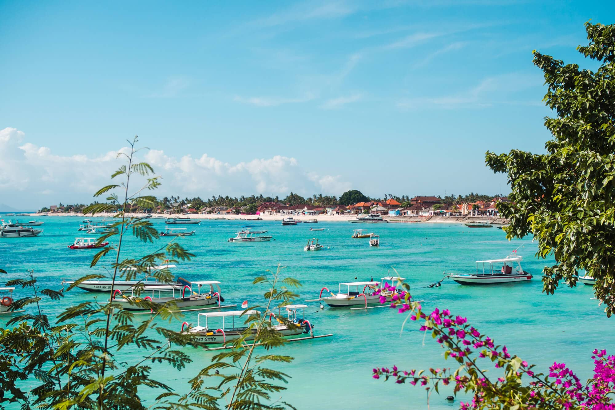 View of a turquoise bay dotted with boats and Jungut Batu Beach in the background on a day trip to Nusa Lembongan from Bali.