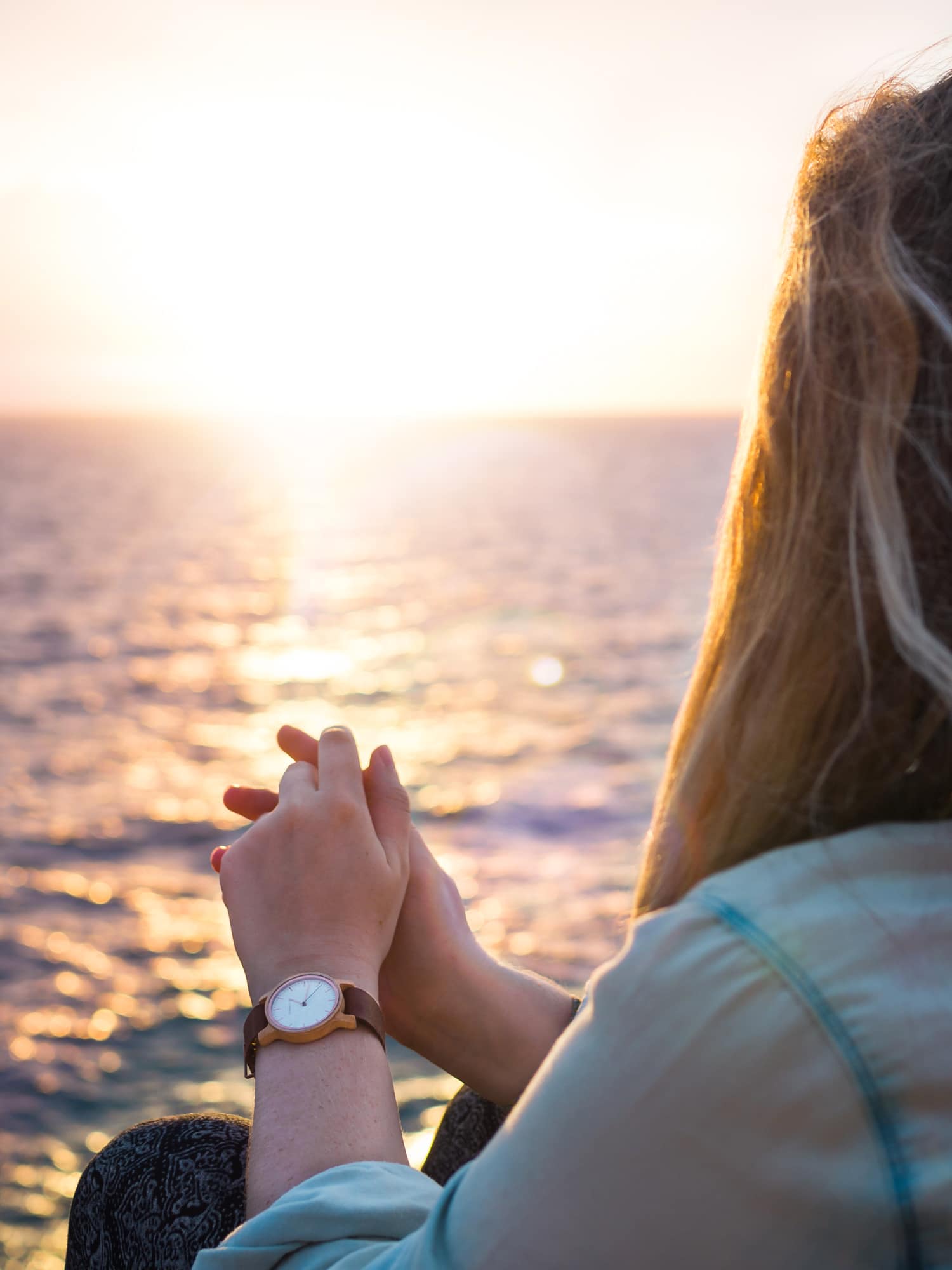 Close up of girl in a denim shirt wearing a brown leather watch looking out over the ocean at the sunset on Koh Samet.