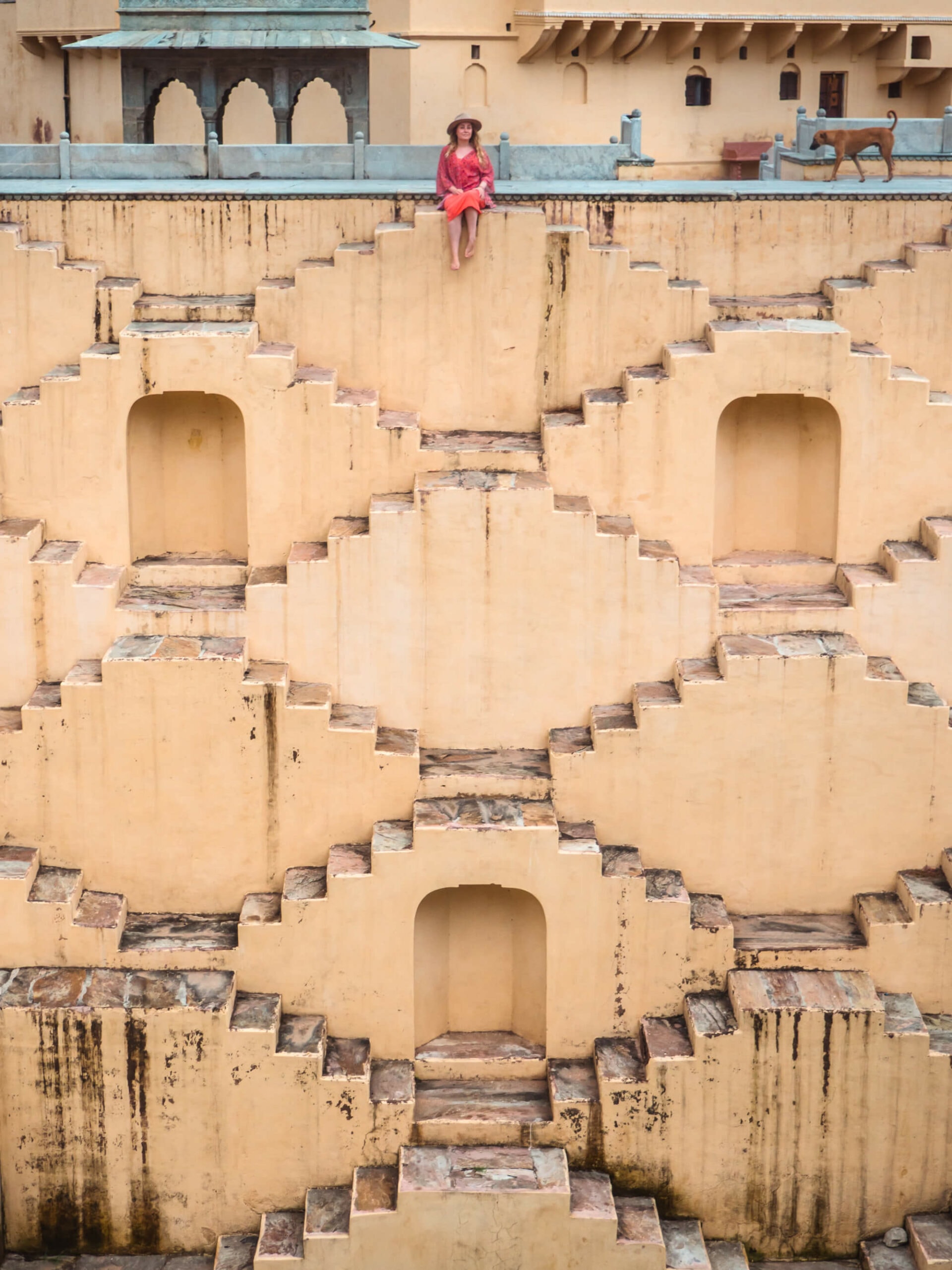 Girl in a pink dress and kimono sitting on top of the Panna Meena ka Kund stepwell, a must on any 2-day Jaipur itinerary.