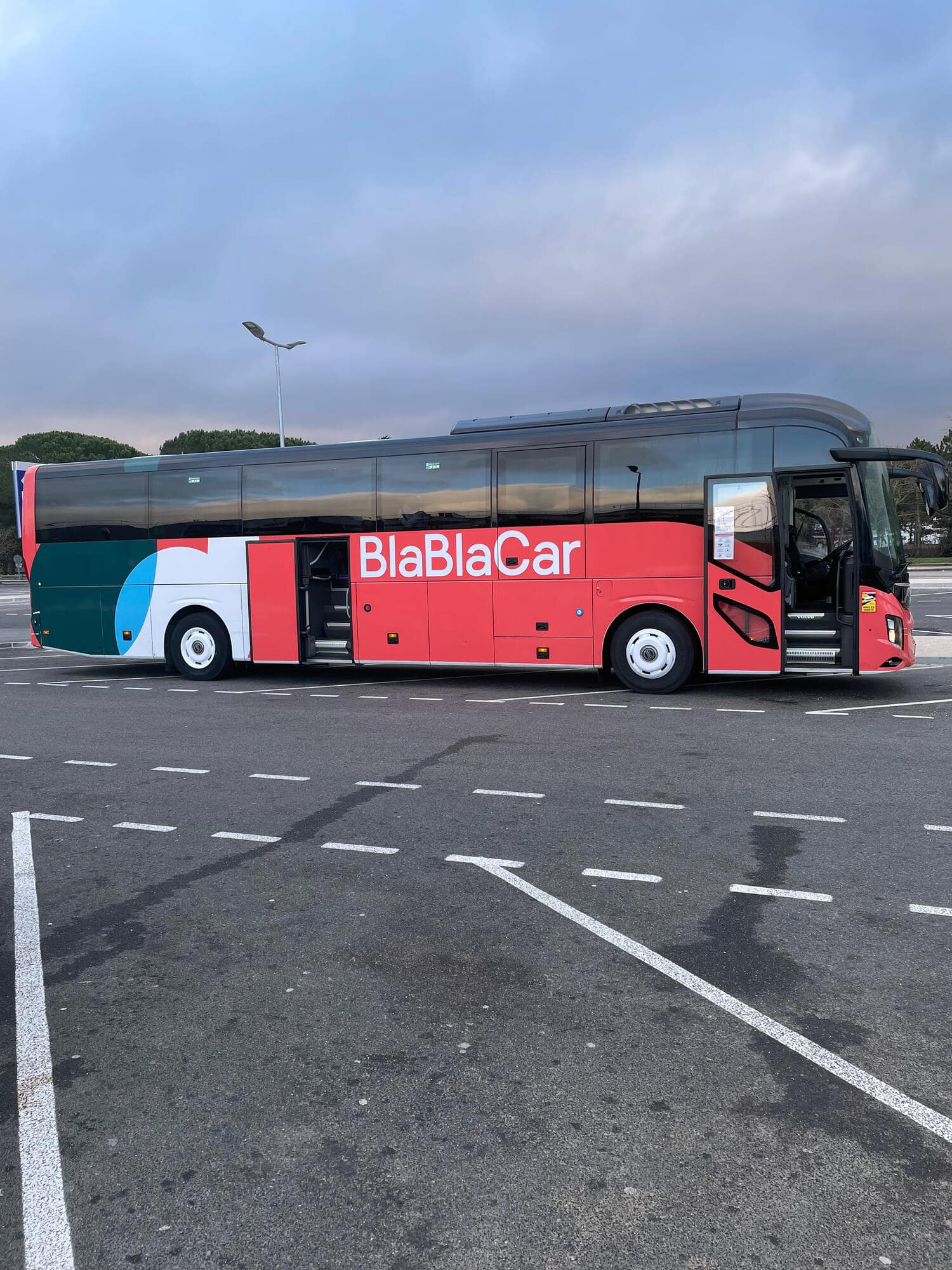 A red, blue and white BlaBlaCar Bus alone on a parking lot at dusk.