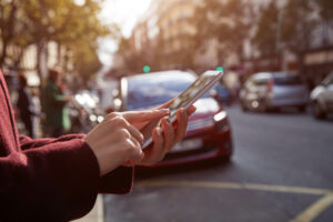 Close up of woman'n hands ordering a BlaBlaCar Rideshare on her phone, with a big city scape int he background