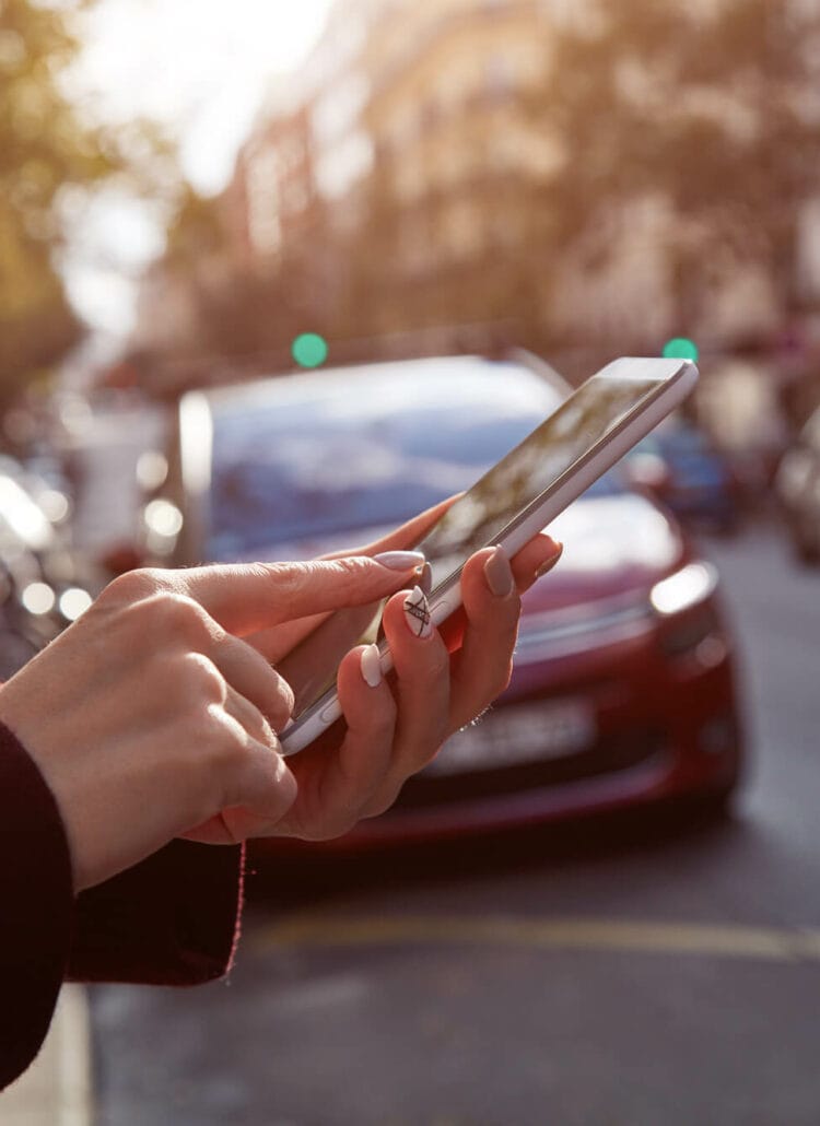 Close up of woman'n hands ordering a BlaBlaCar Rideshare on her phone, with a big city scape int he background