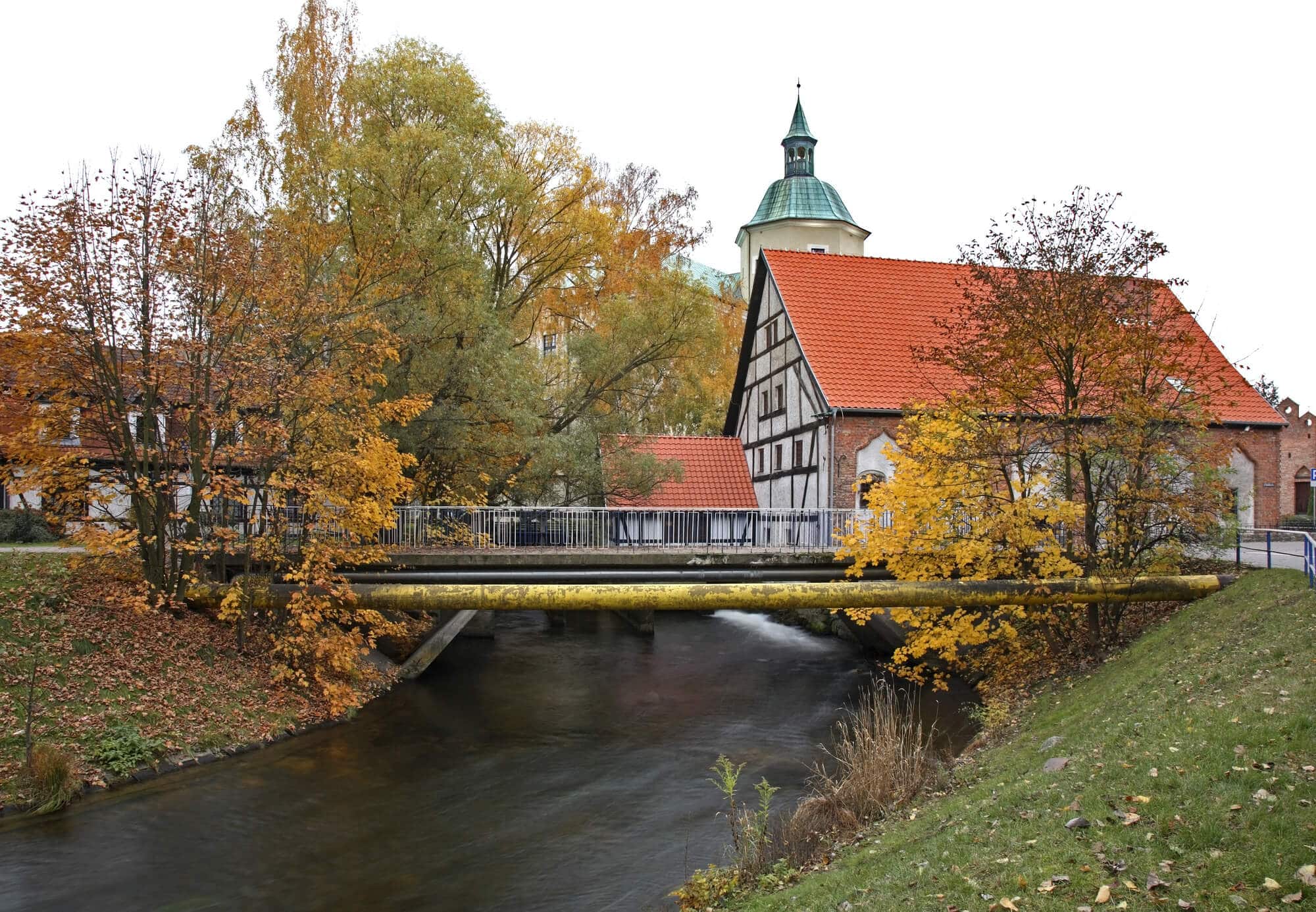 A bridge over a river with an old tudir style house in the background in Slupsk, a great day trip from Gdansk.