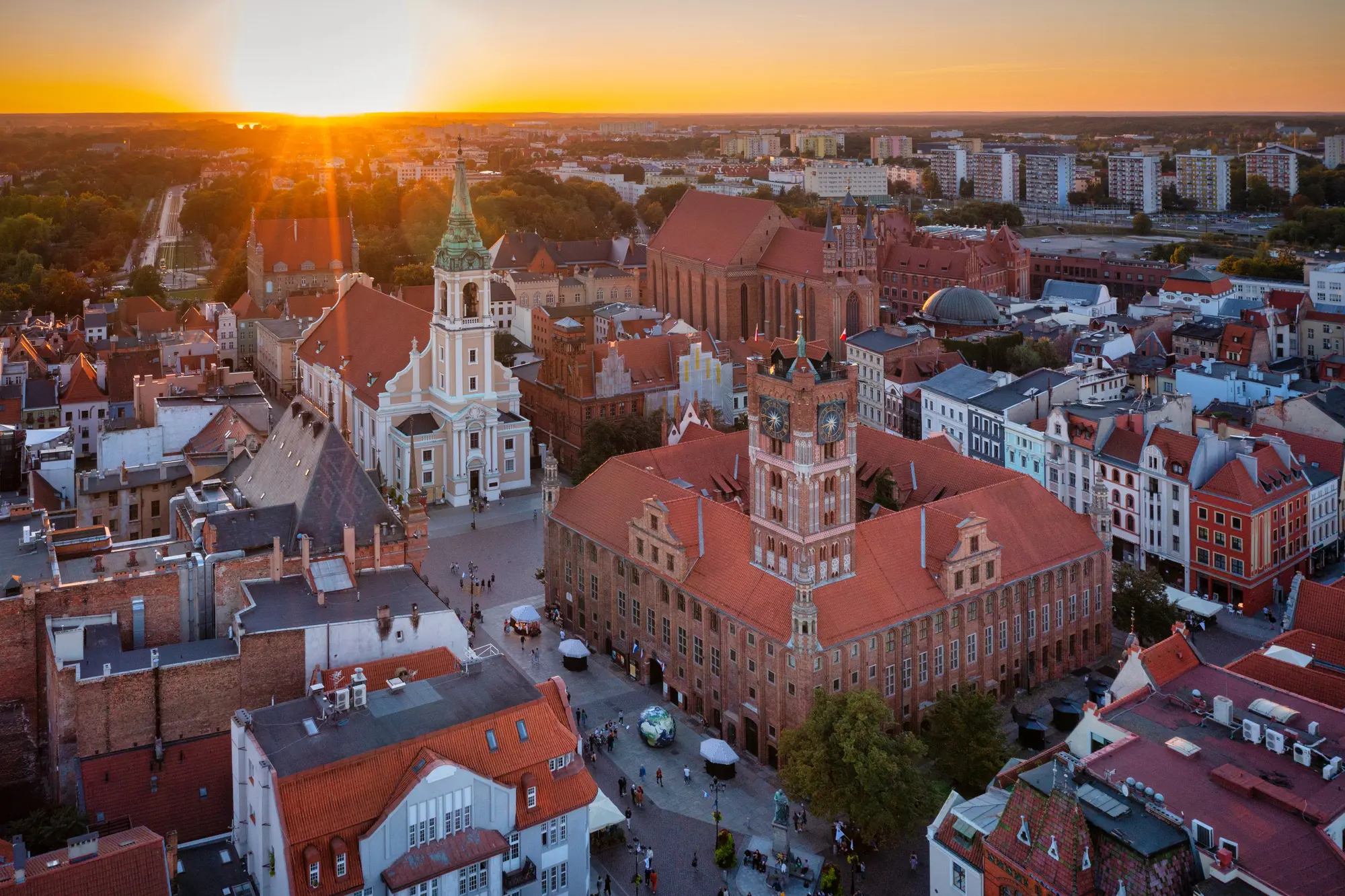 Sun setting over the white and beige cathedral and brick market square in Torun on a day trip from Gdansk.