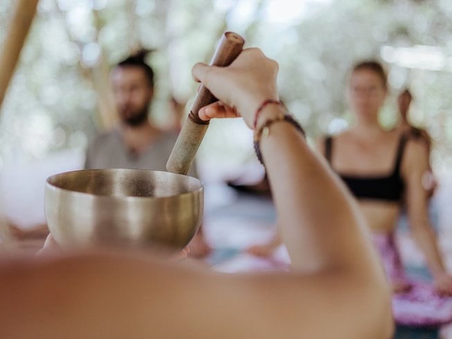 Close up of a woman holding a sound bowl with yogis sitting on their mats blurry in the background, during a surf and yoga retreat in Bali.