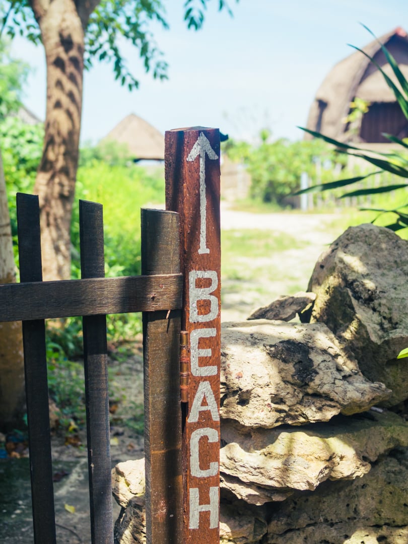 Close op of a gate on Nusa Lembongan with a painted sign in white letters reading BEACH and an arrow, greenery in the background. A must during your two week Bali itinerary.
