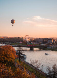 Is Poland worth visiting? View of the river in Krakow with a hot air balloon, ferris wheel and bridge from Wawel Castle at sunset during fall.