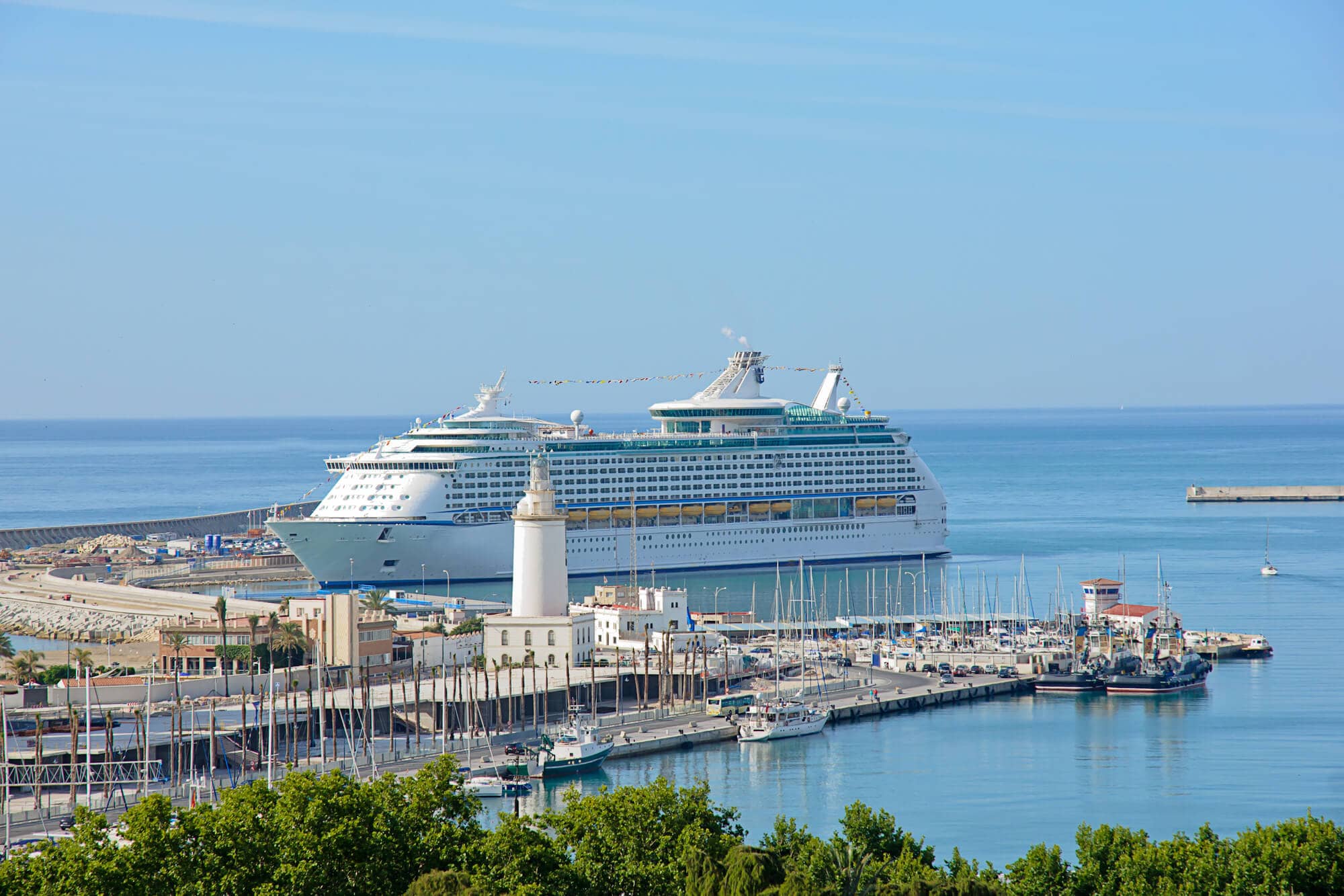 Cruise ship at the dock in Malaga Cruise Port on a sunny clear day with a small lighthouse in the foreground.