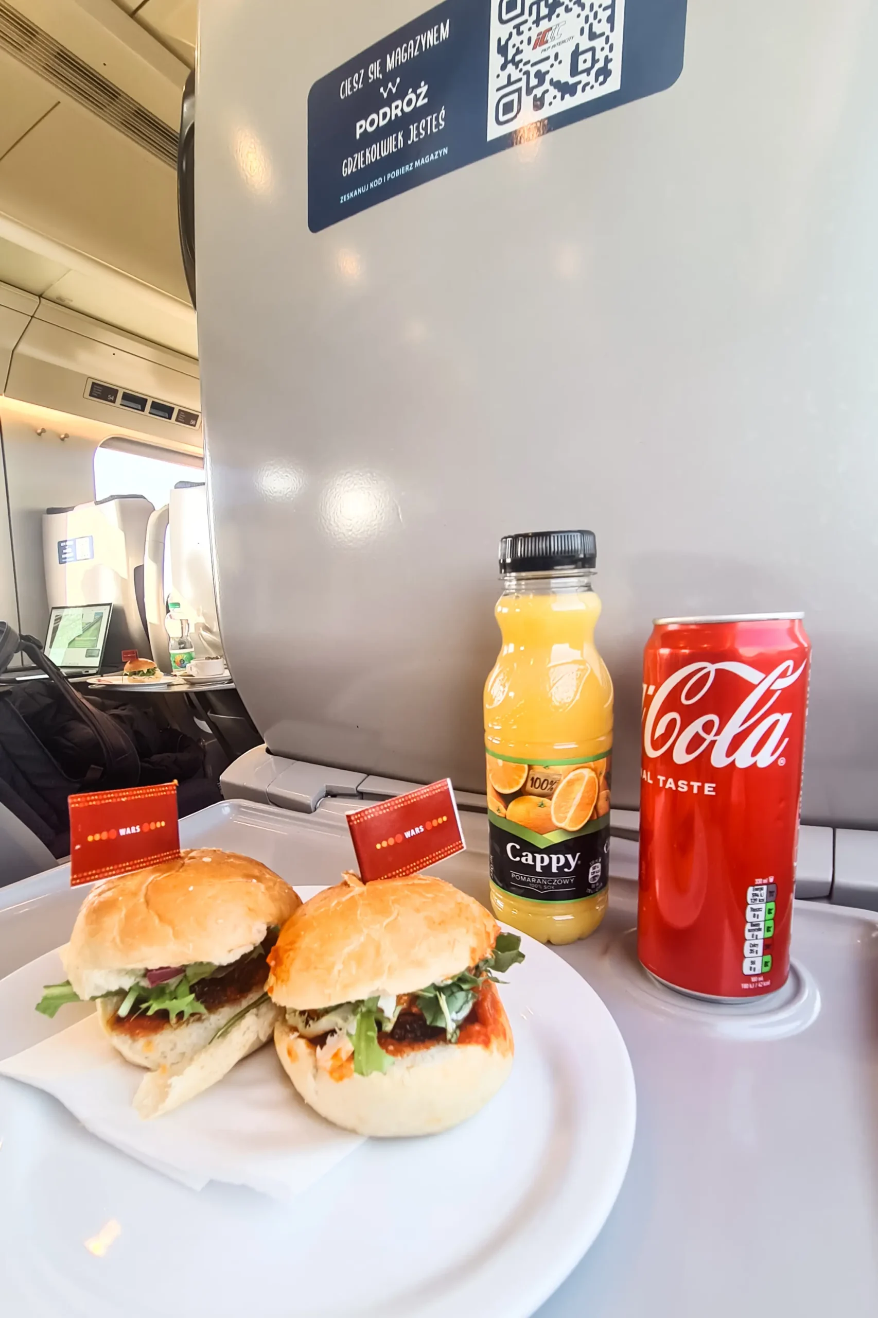 Two sandwiches, red coke can and an orange juice on a tray table during a train ride in Poland.