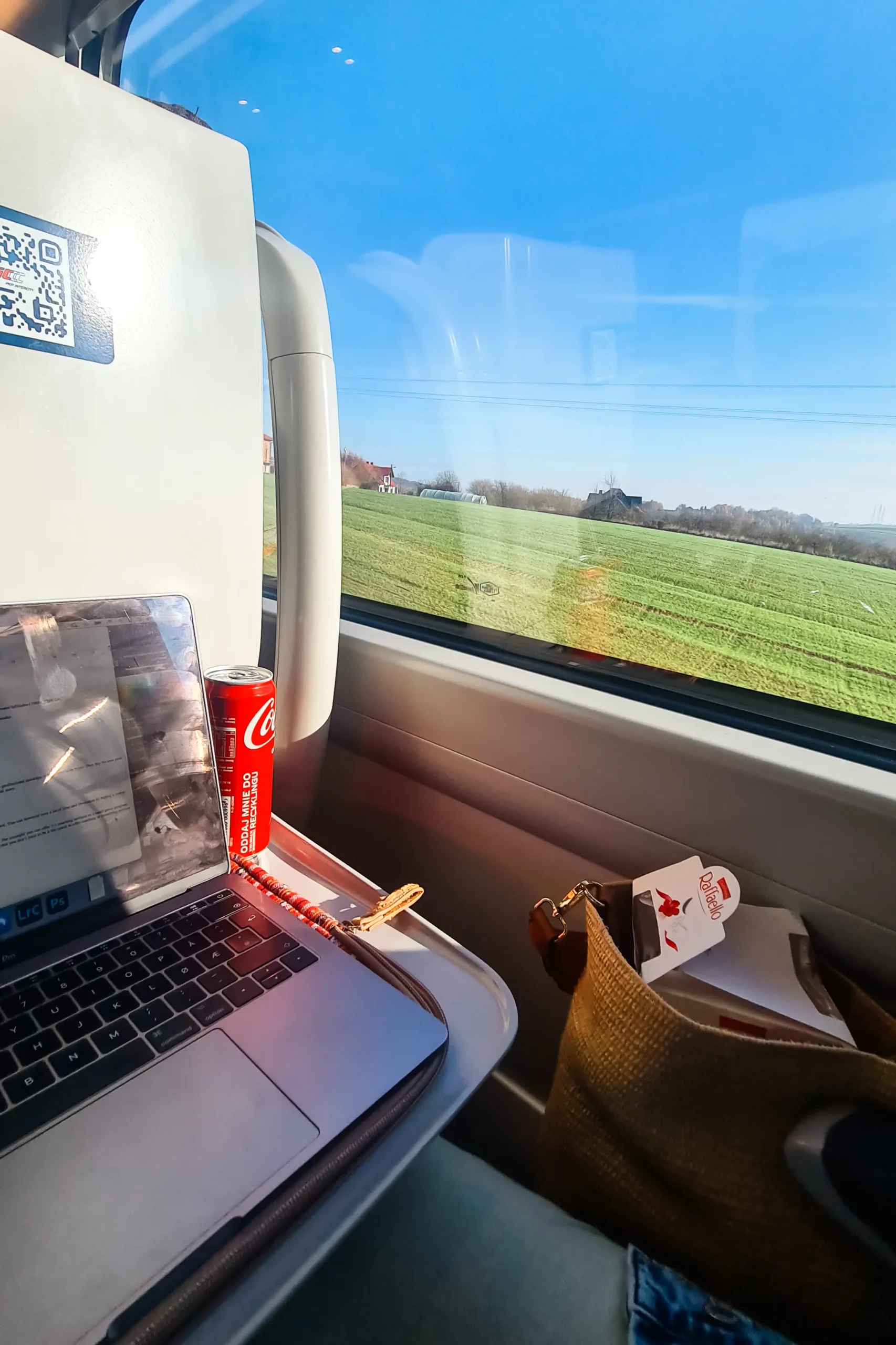 Computer and a red coke can on a tray table in a train by the window on a sunny day in Poland.