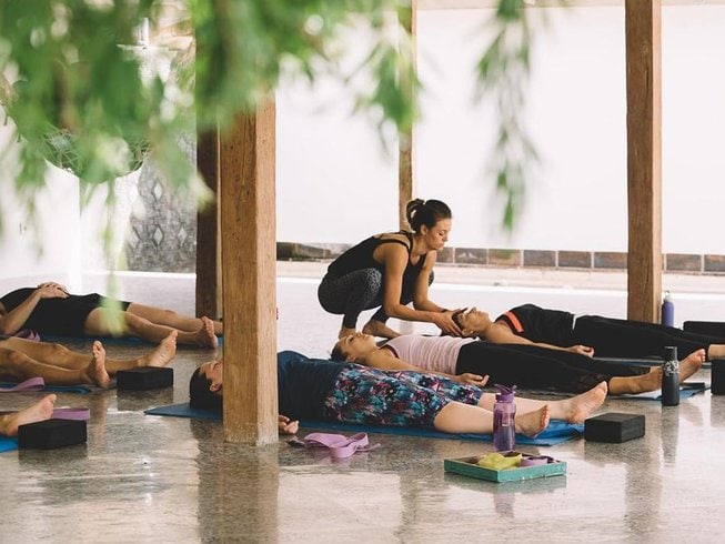 People laying on yoga mats on the floor in an open air yoga shala during a surf and yoga retreat in Bali.
