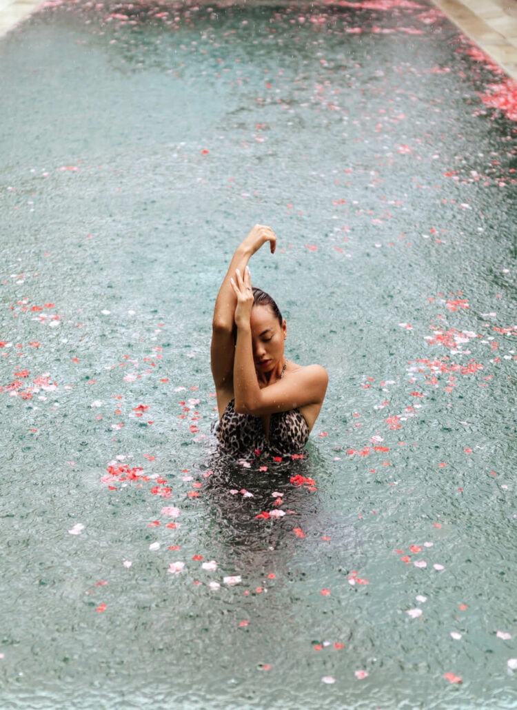 Woman standing in a pool. with pink flower petals in Bali during the rainy season.