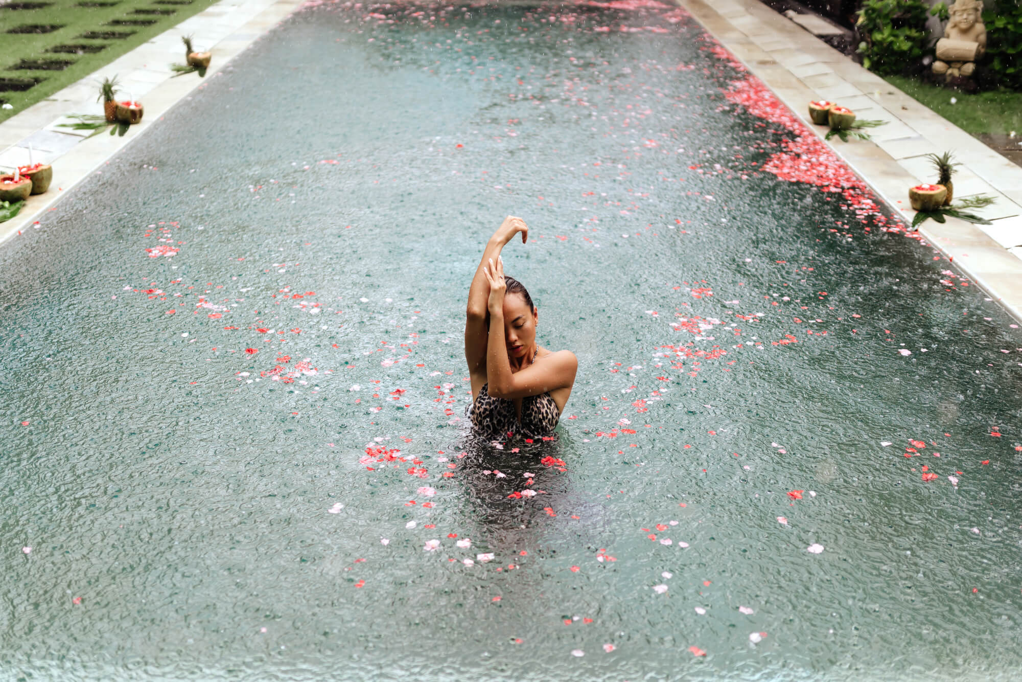 Woman standing in a pool. with pink flower petals in Bali during the rainy season.