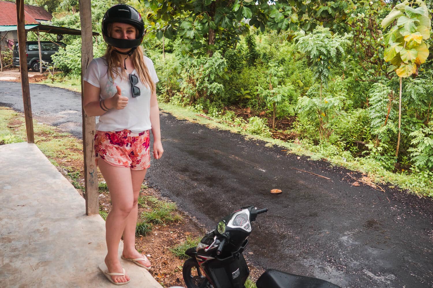 Girl wearing a pink shorts, white t-shirt and black helmet, taking shelter from the rain on Nusa Lembongan during the wet season in Bali.