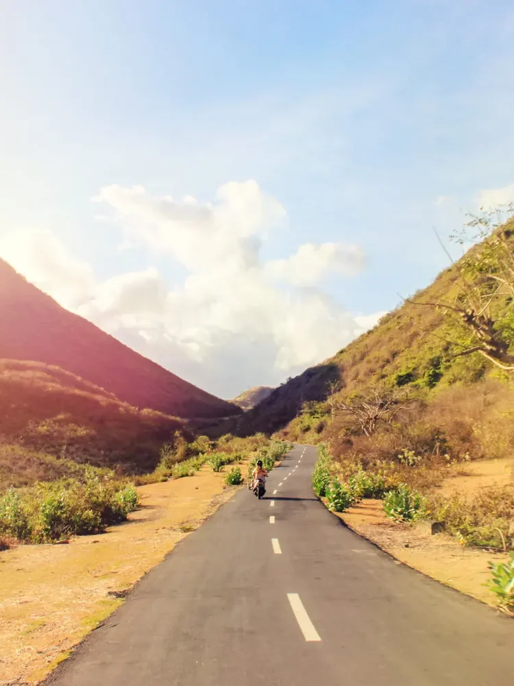 Woman riding a scooter on a narrow road between two hillsides during a warm sunset in Kuta Lombok, covered by SafetyWing Nomad Insurance 2.0.