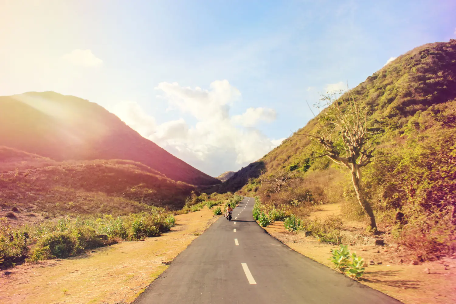 Woman riding a scooter on a narrow road between two hillsides during a warm sunset in Kuta Lombok, covered by SafetyWing Nomad Insurance 2.0.