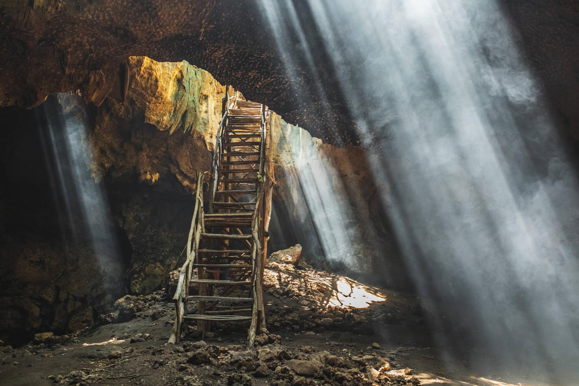 Makeshift bamboo stairs leading into Bangkang Cave with light rays coming in in several places, one of the top things to do in Lombok.