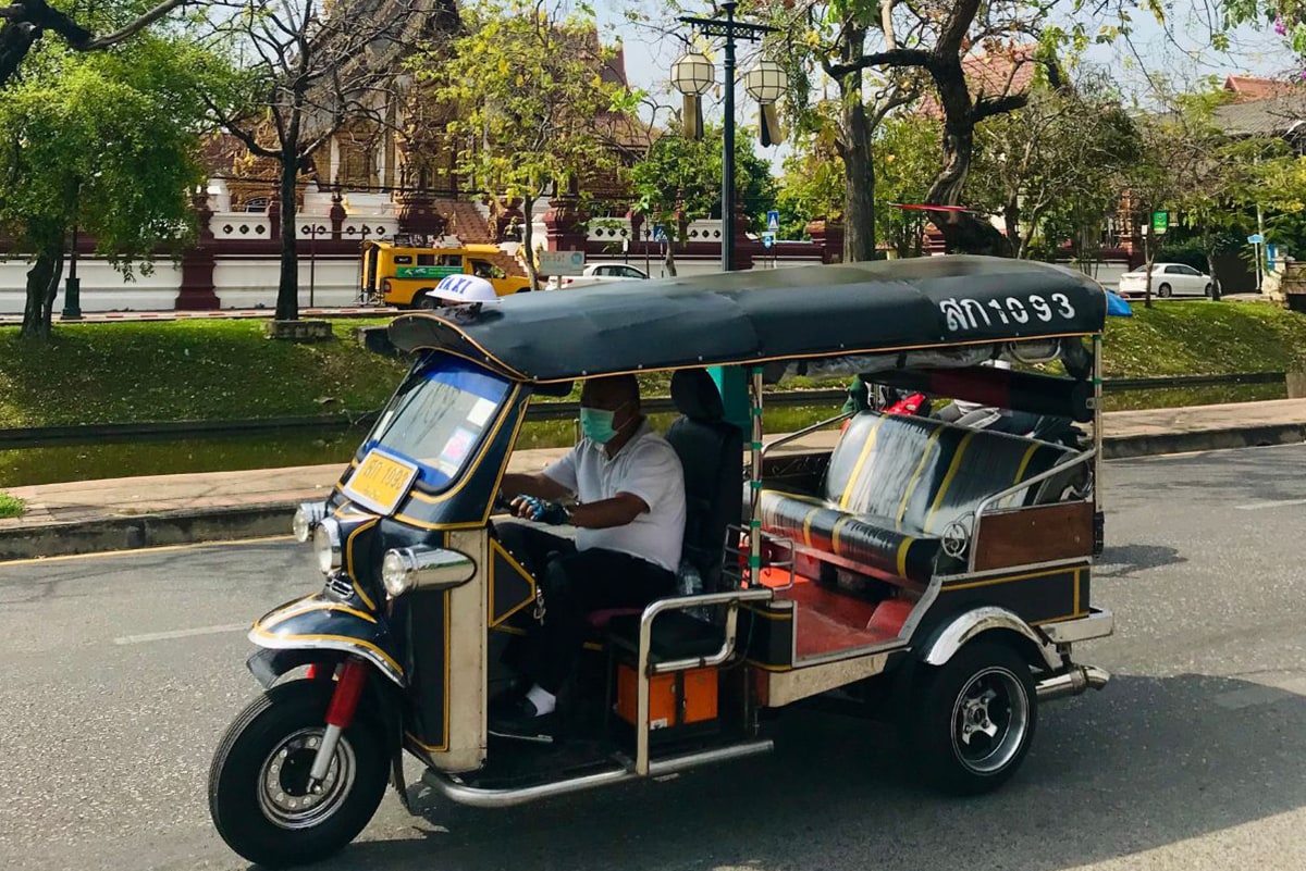 Typical tuk tuk with black roof and two seats in the back on the streets of Chiang Mai, going from temple to temple.