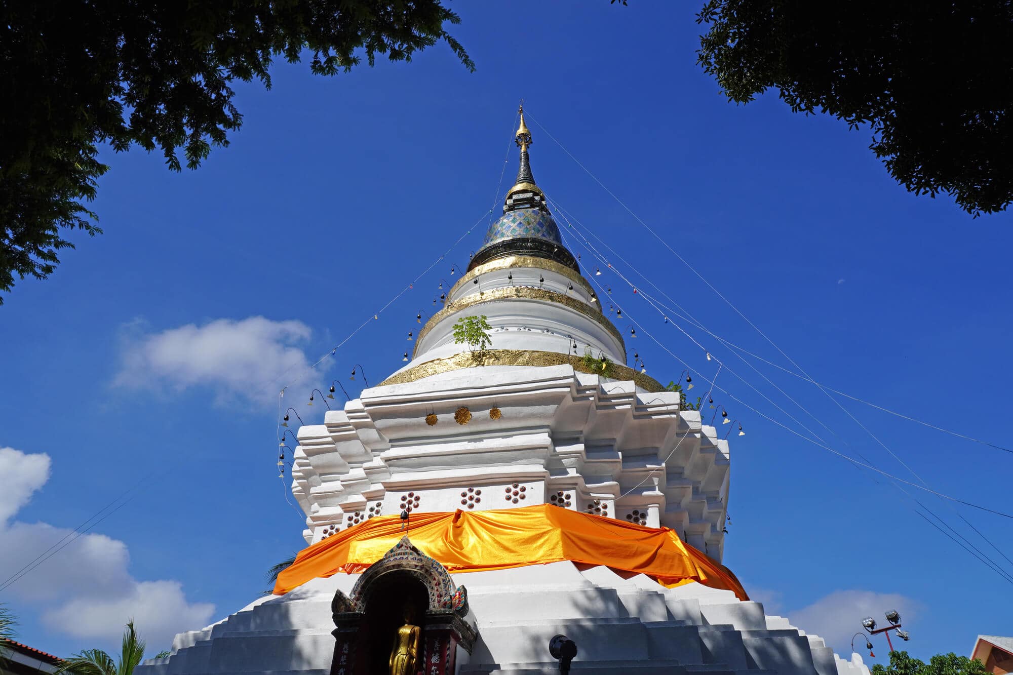 White chedi decorated with an orange silk fabric at Wat Ket Karam temple set againt a blue sky in Chiang Mai.