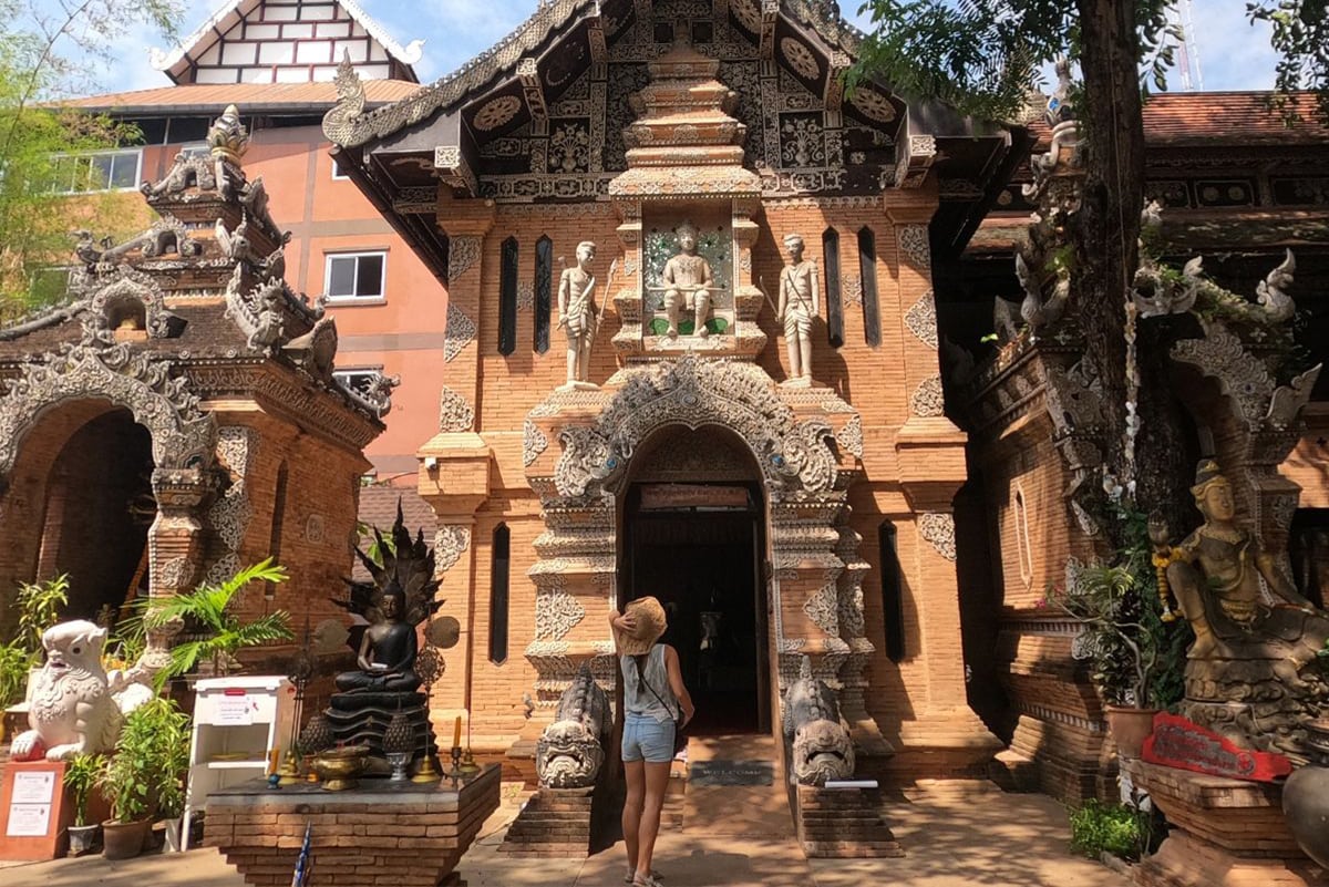 Girl wearing a hat and denim shorts looking up at the orange colored Wat Look Moli, one of the best temples in Chiang Mai.