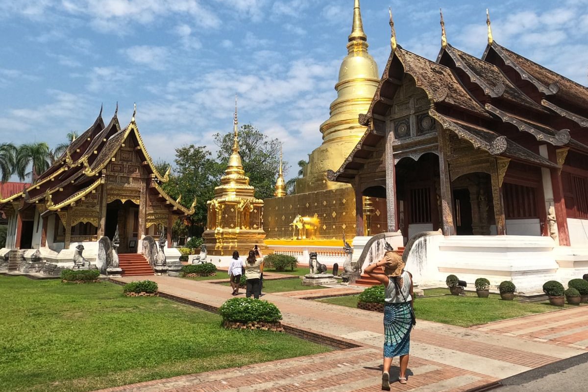 Girl wearing a hat and a green sarong walking towards Wat Phra Singh, with a large gold chedi in the background, one of the most beautiful temples in Chiang Mai.