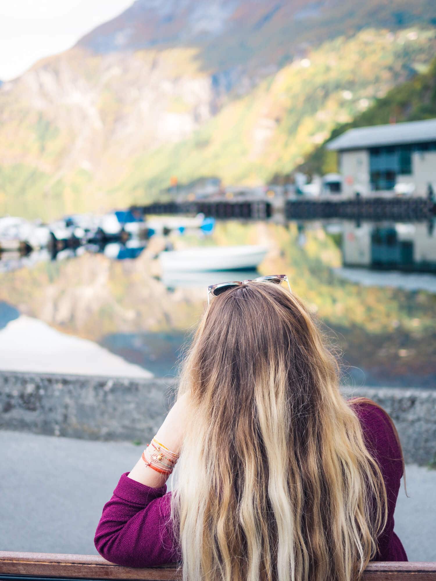 Girl with long hair, wearing a purple sweater, looking out at the water in Geiranger, a free things to do that keeps the travel cost in Norway down.