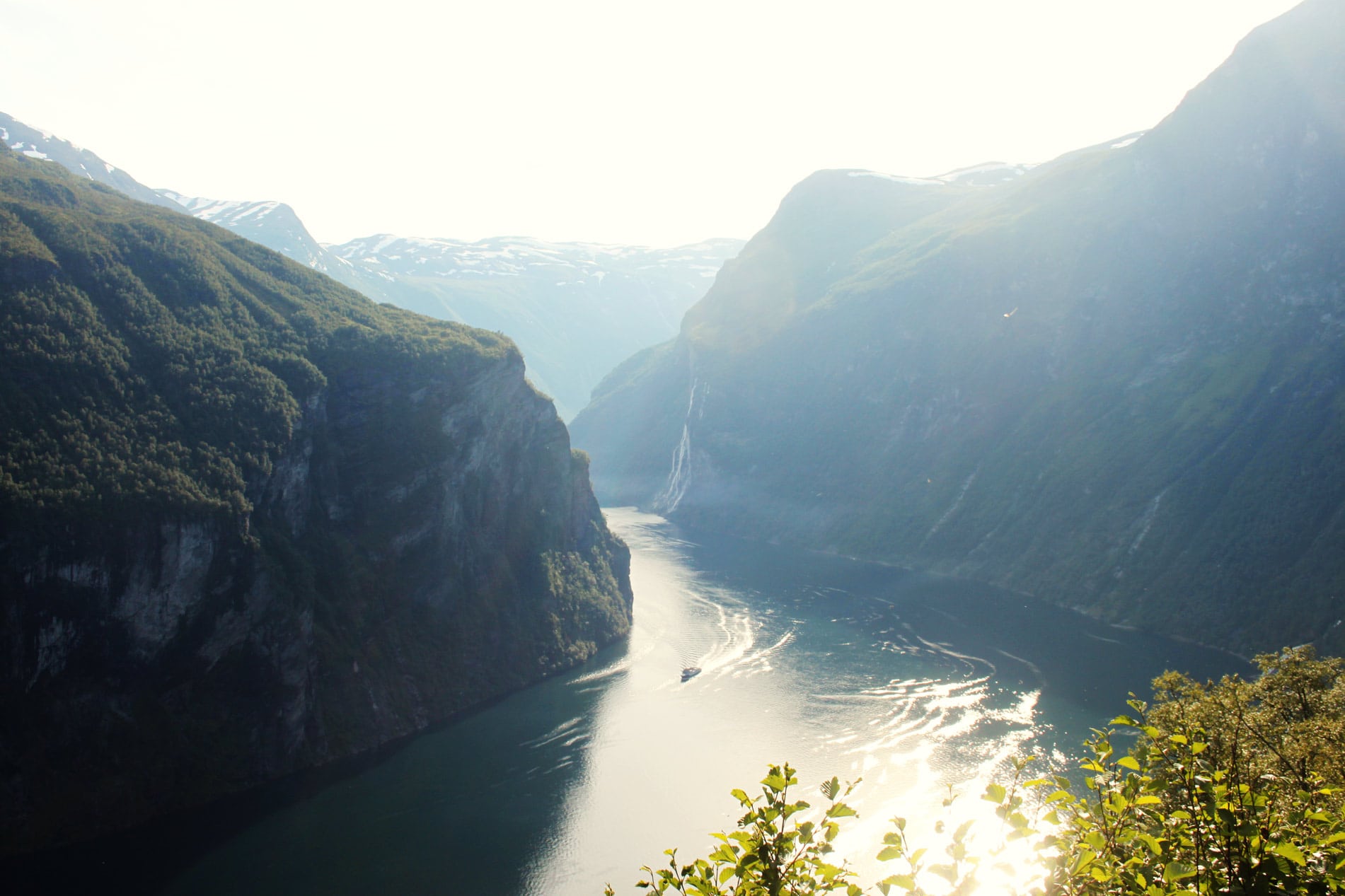 View from above of a boat on the Geirangerfjord between two mountains in the sunlight. Fun facts Norway.