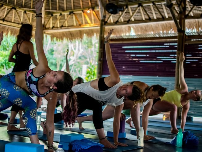 Women on blue mats practicing yoga in a bamboo shala during a wellness retreat, one of the top things to do in Lombok.