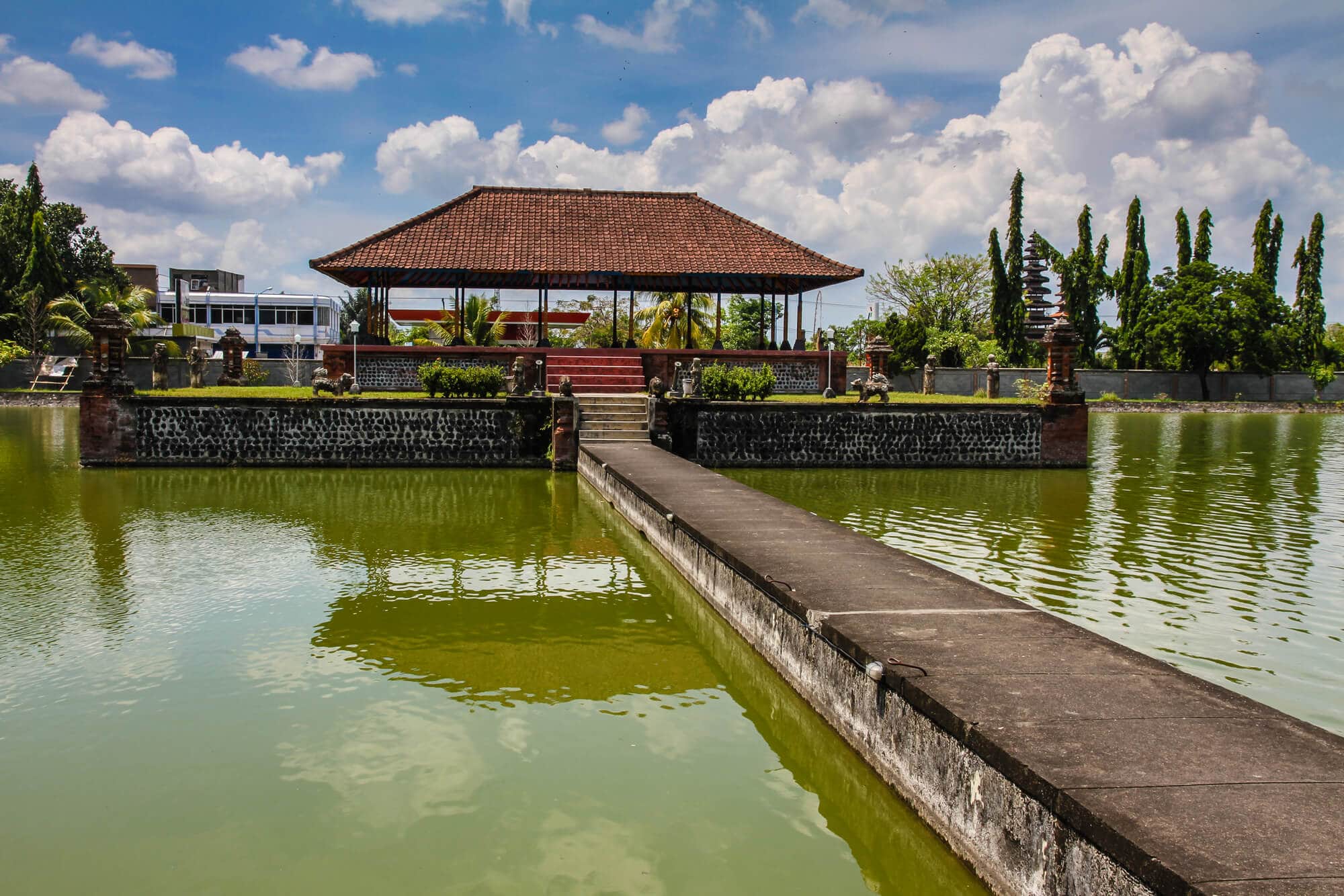 Mayura Water Palace surrunded by green water with a stone walkway leading to it, one of the top sights to see in Lombok.