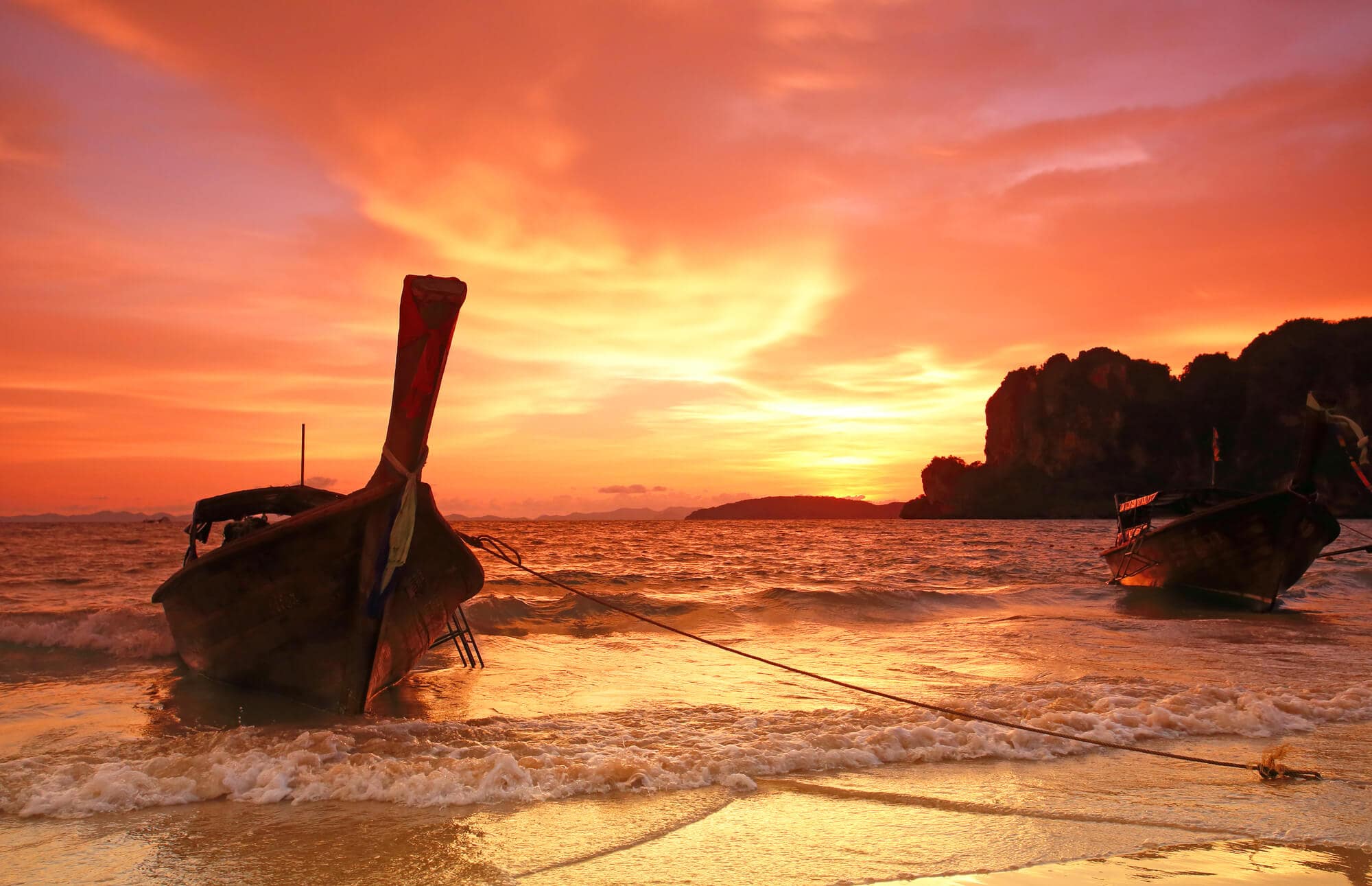 Traditional Thai wooden boat at the beach in Krabi during a red and yellow sunset on a day trip from Krabi.