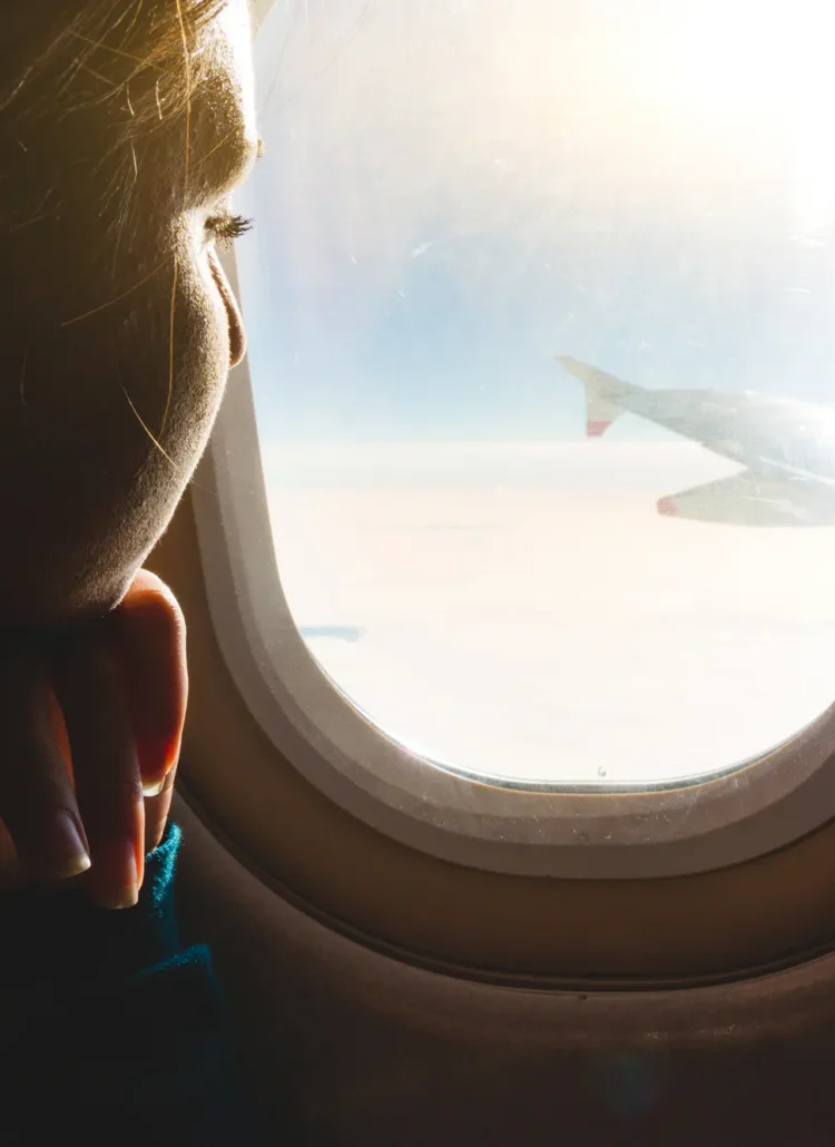 Close up of woman looking out the window on the wing of an airplane with sunlight shining in. Tips for coping with and overcoming fear of flying.