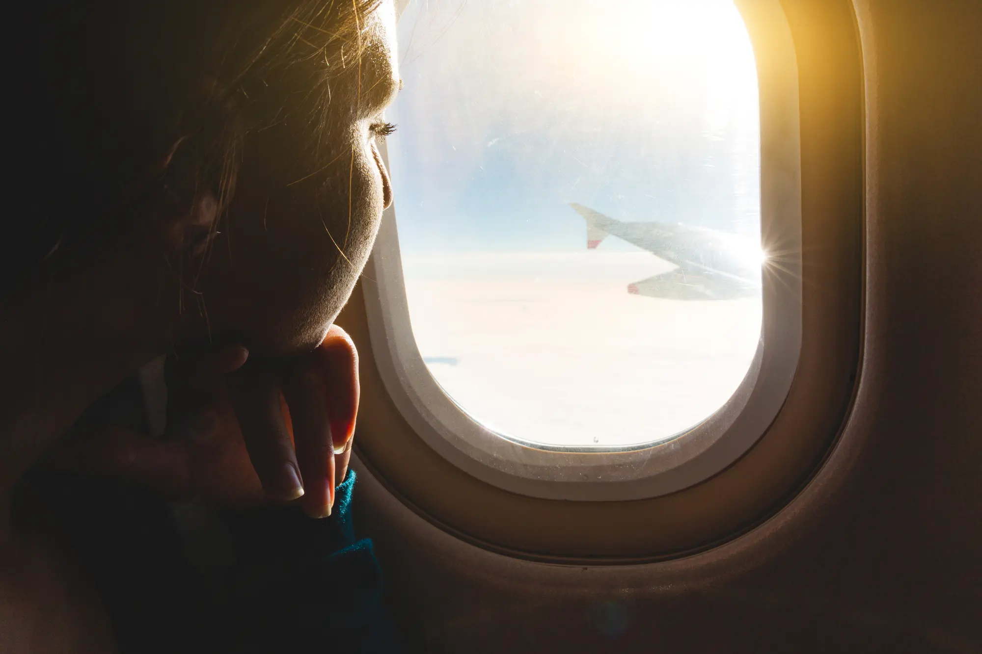 Close up of woman looking out the window on the wing of an airplane with sunlight shining in. Tips for coping with and overcoming fear of flying.