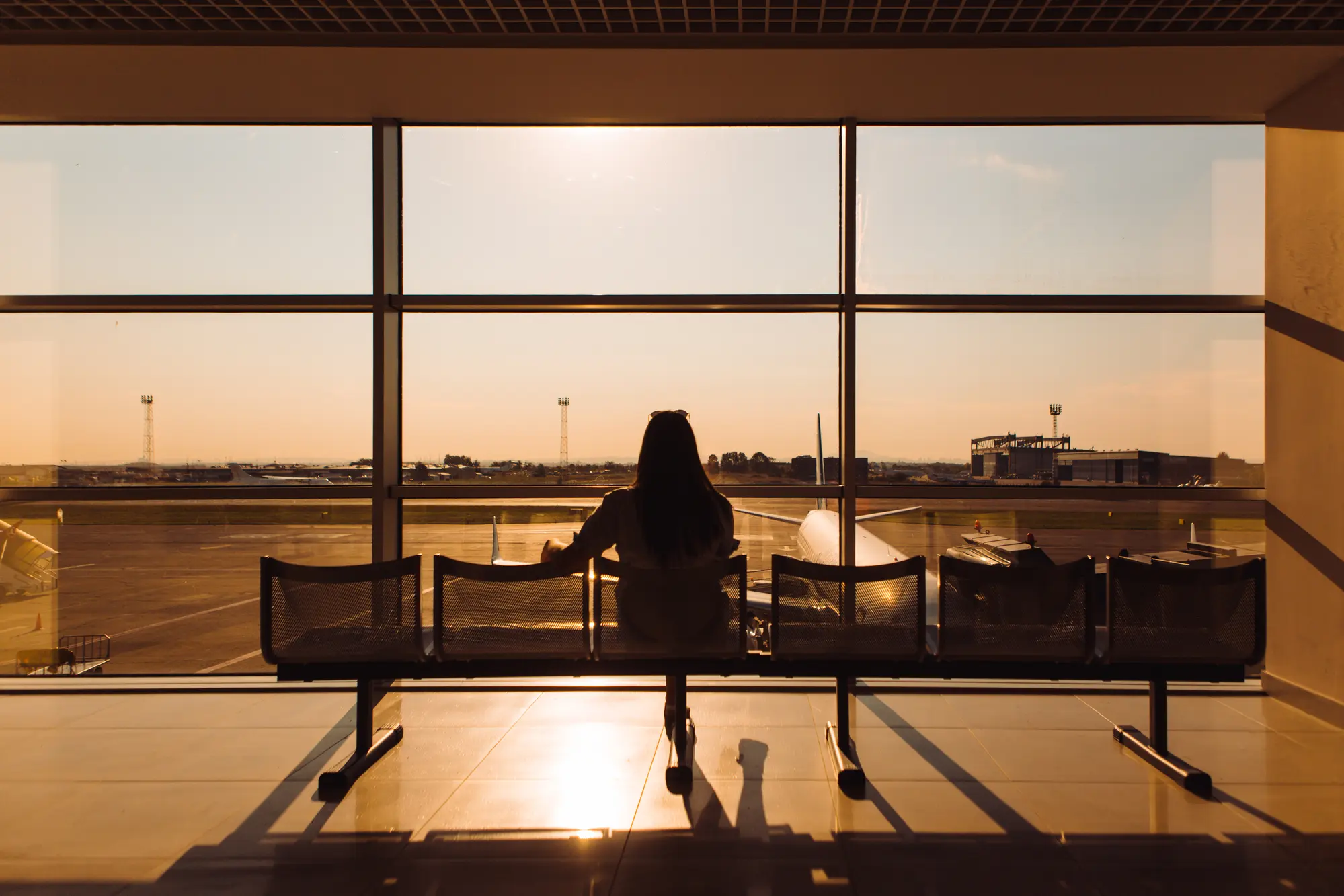 Woman sitting alone at an airport gate looking out a large window during sunset. How to overcome fear of flying tips.