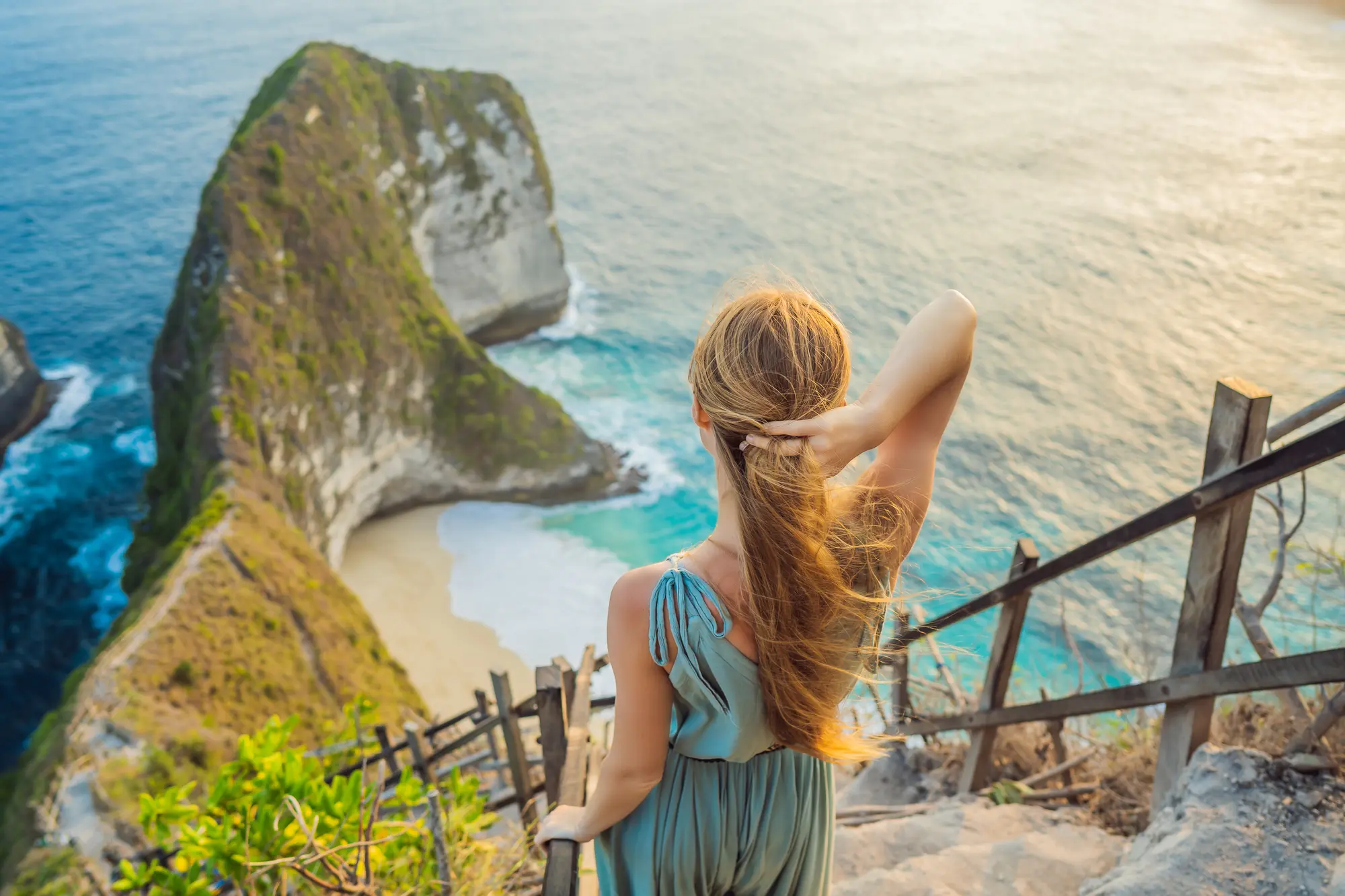 Girl holding her hair in the wind standing on the top of the steep stairs at Kelingking Beach during a 1-day itinerary in West Nusa Penida.