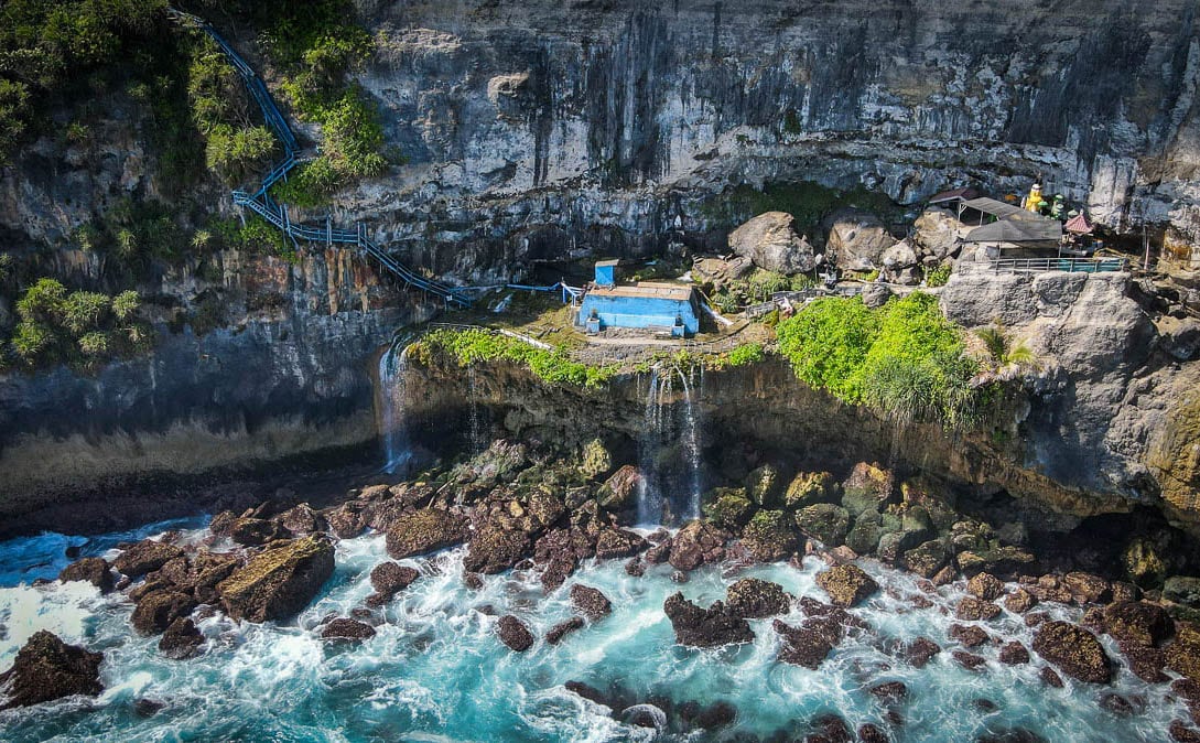 Blue stairs, small waterfalls and temple at the bottom of a cliff by the ocean at Peguyangan Waterfall in West Nusa Penida.