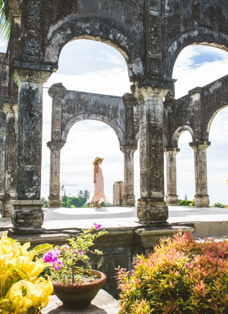 Girl in a flowing dress and hat on a platform with arches in Taman Ujung Water Palace in Bali.