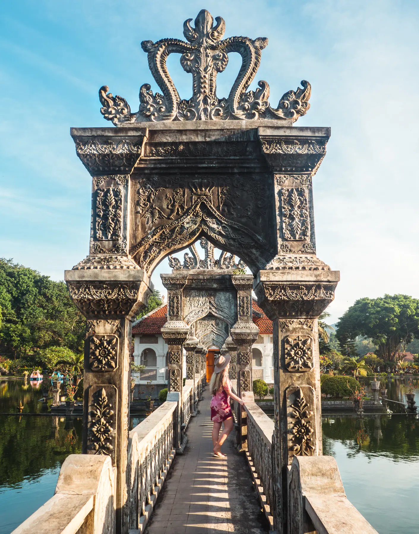 Girl in a purple dress standing on a stone bridge with arches, looking out over the waters, in Taman Ujung Water Palace during sunrise.